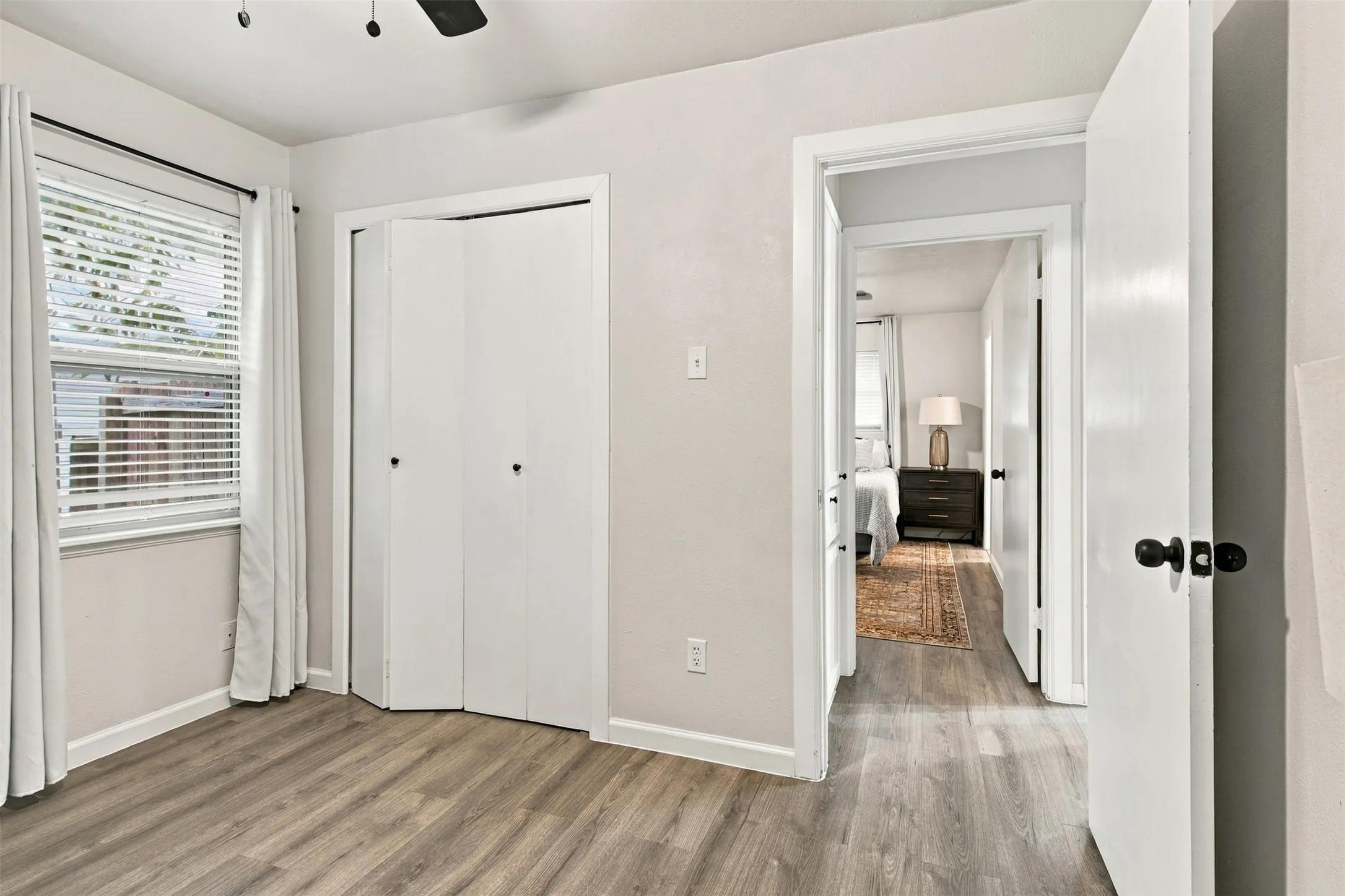 Wood-finish flooring, white walls, and a window with blinds