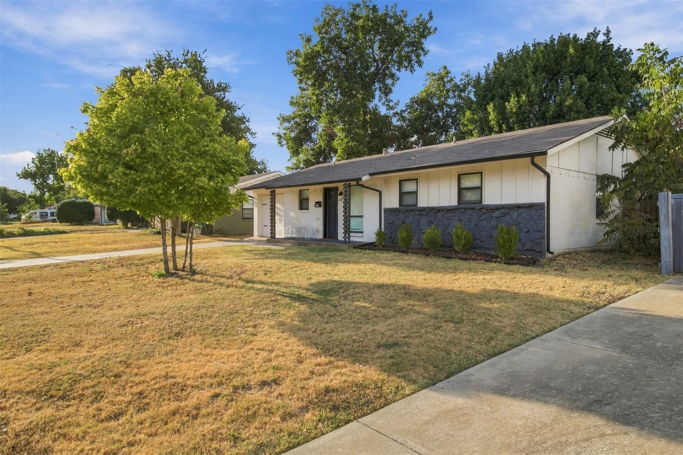 White exterior with black accent wall, asphalt shingle roof, and established landscaping