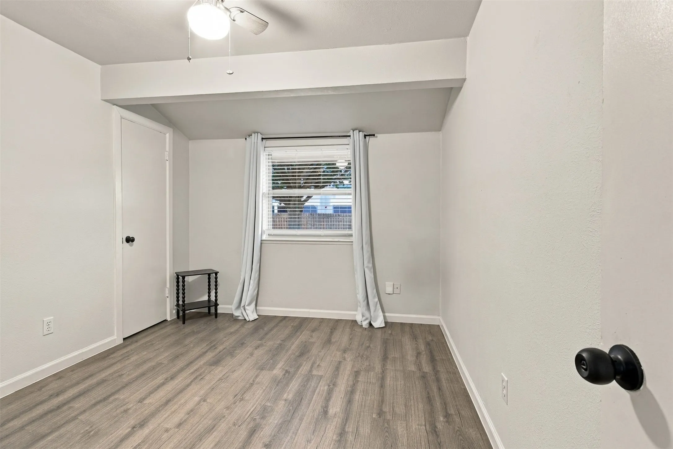 Wood-finish flooring, white walls, and a ceiling fan with integrated lighting