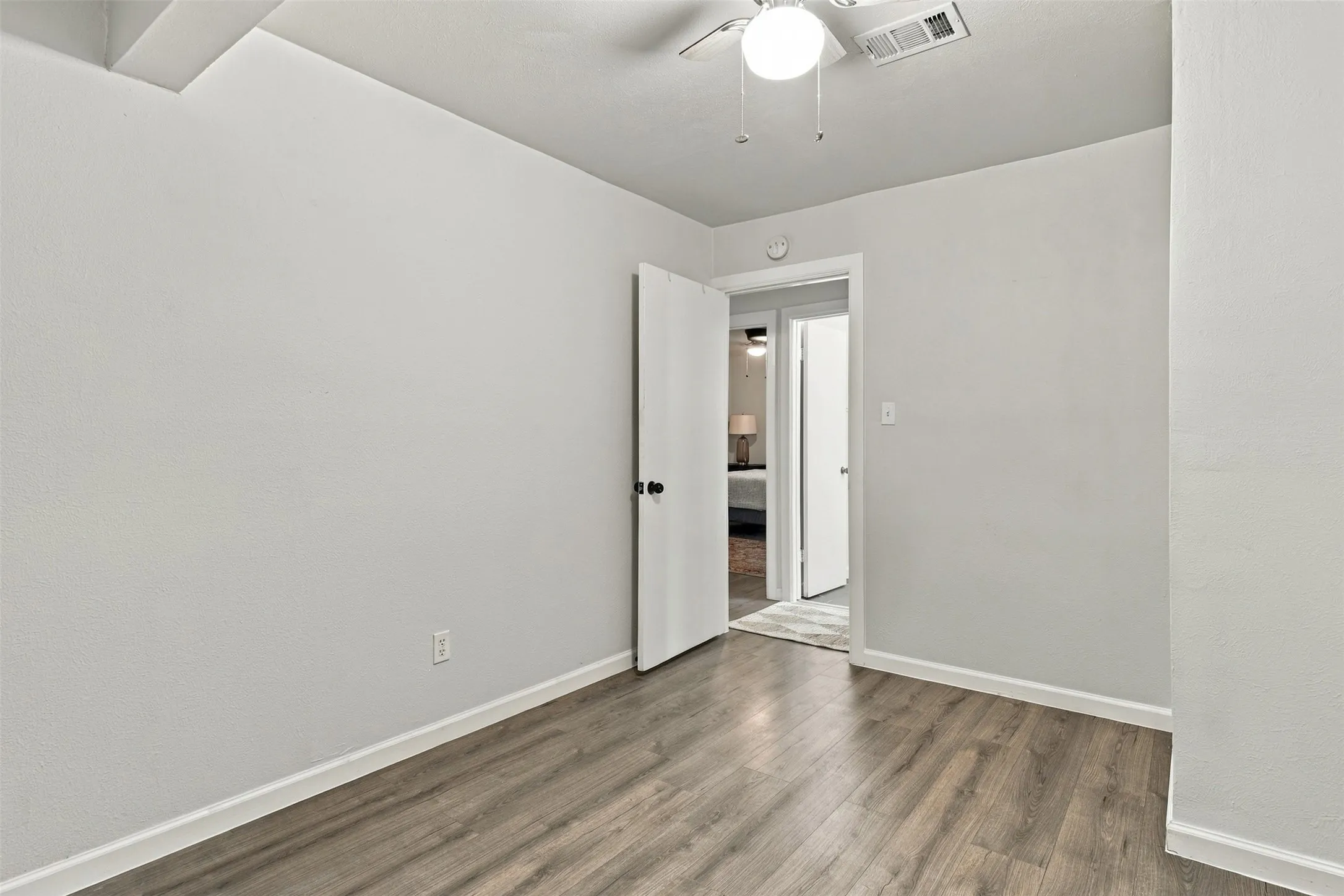Wood-finish flooring with white trim, a ceiling fan with light fixture, and a white interior door with black hardware