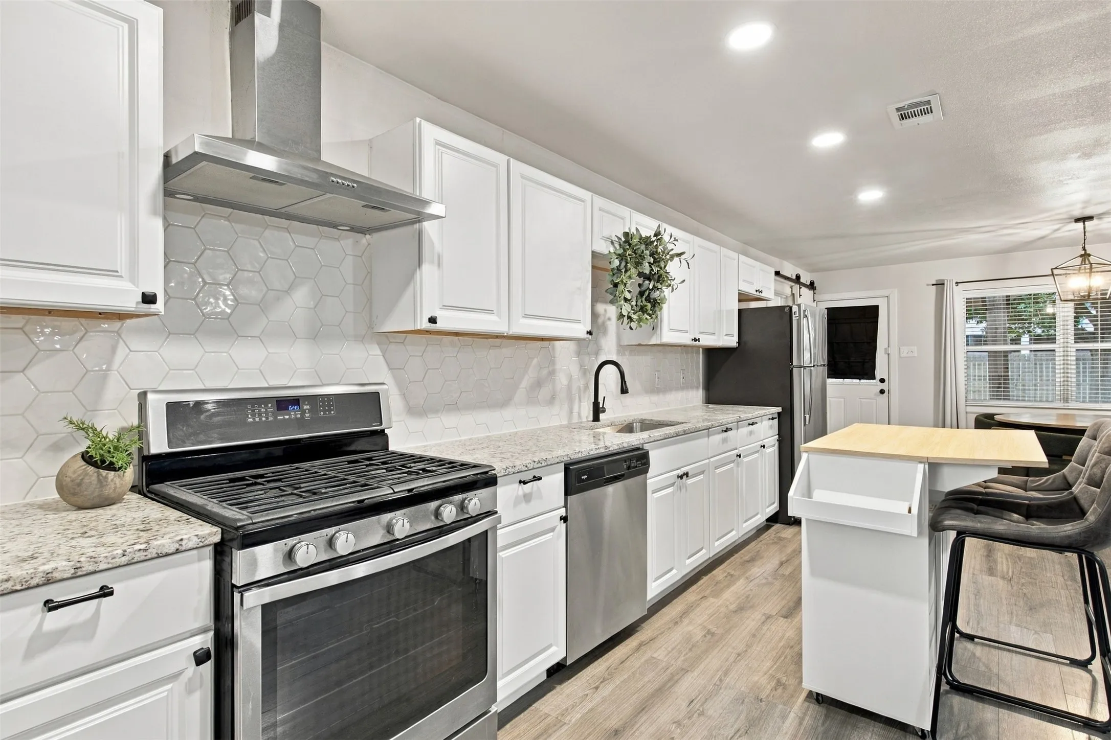 White shaker-style cabinetry, stainless steel appliances, light-toned wood-finish flooring, hexagonal tile backsplash, and recessed lighting