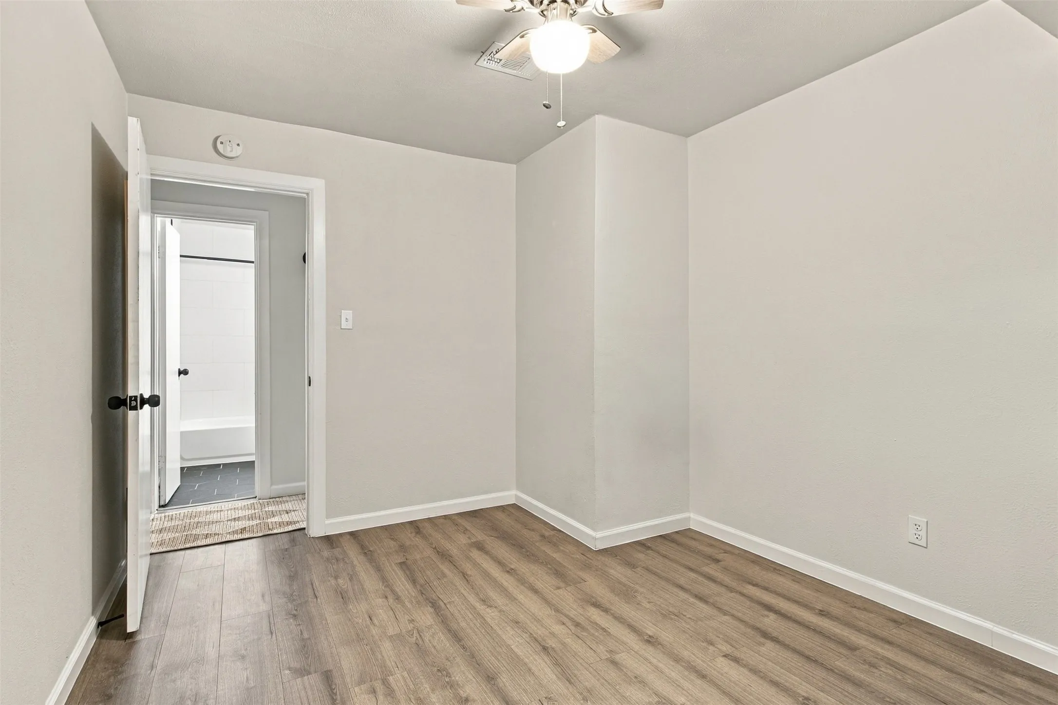 Wood-finish flooring, light-toned wall paint, and a ceiling fan with integrated lighting