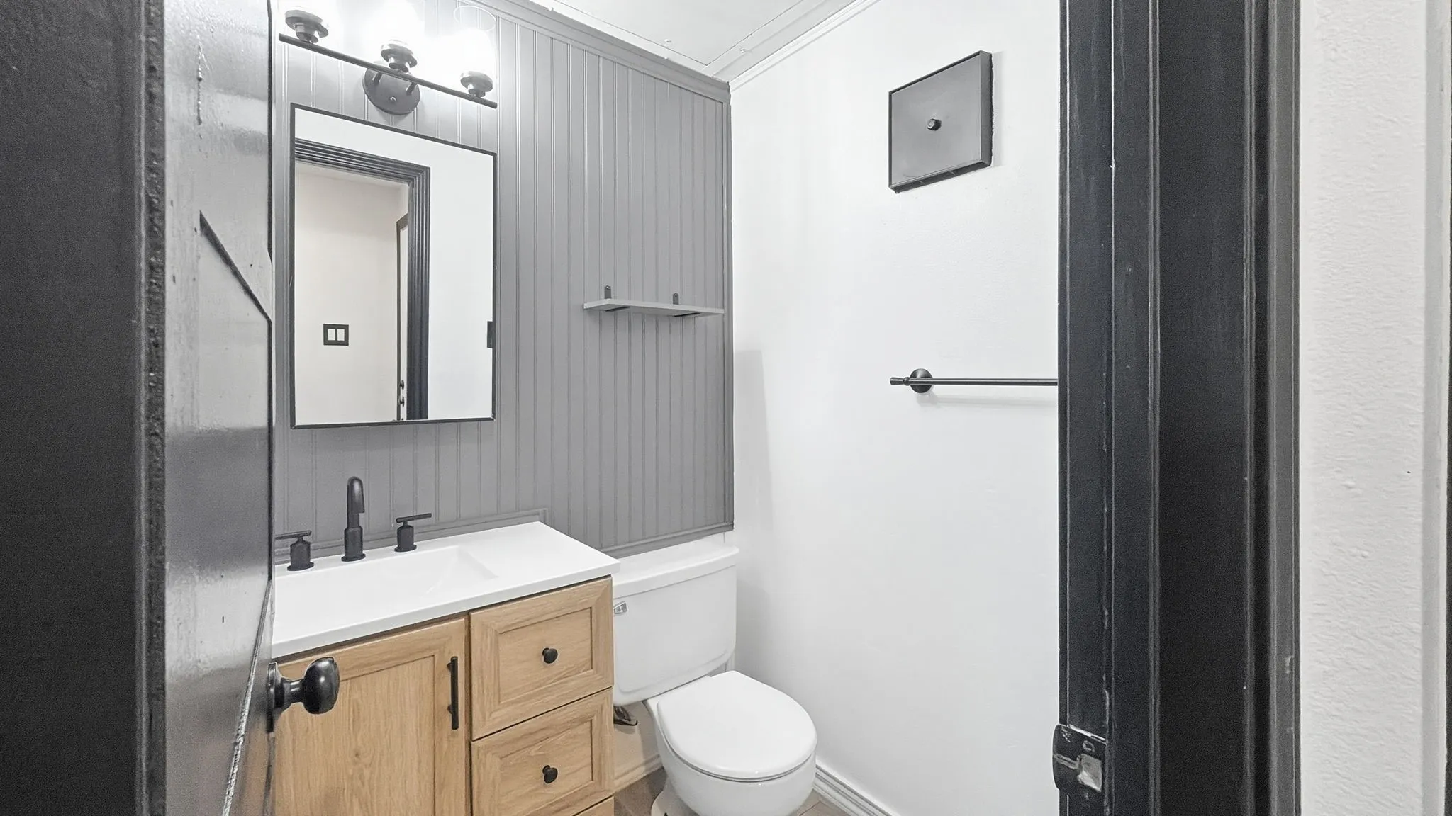 Wood-finish vanity with white countertop, matte black faucet, and rectangular mirror