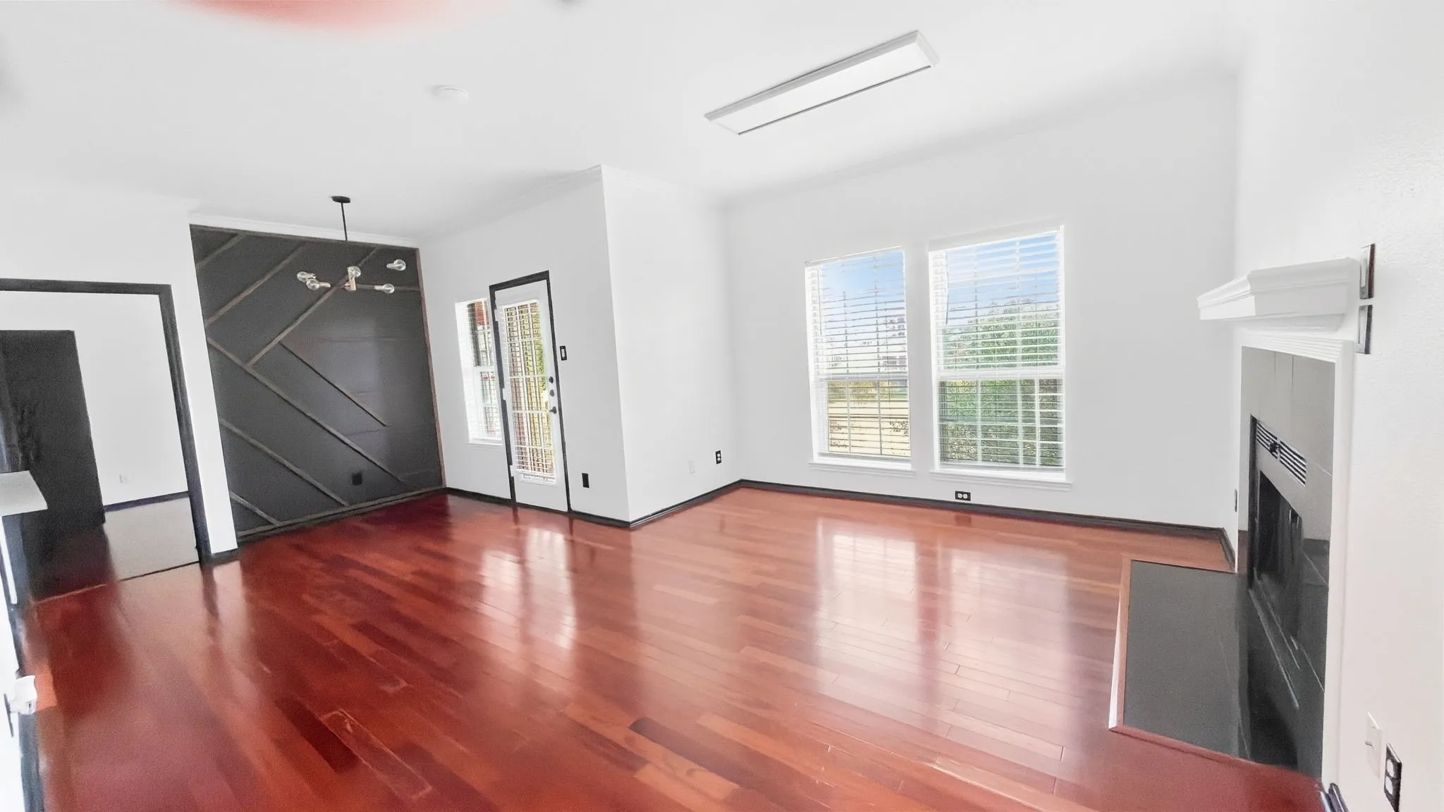 Hardwood flooring throughout, contemporary accent wall, modern chandelier, fireplace with hearth, and multiple windows