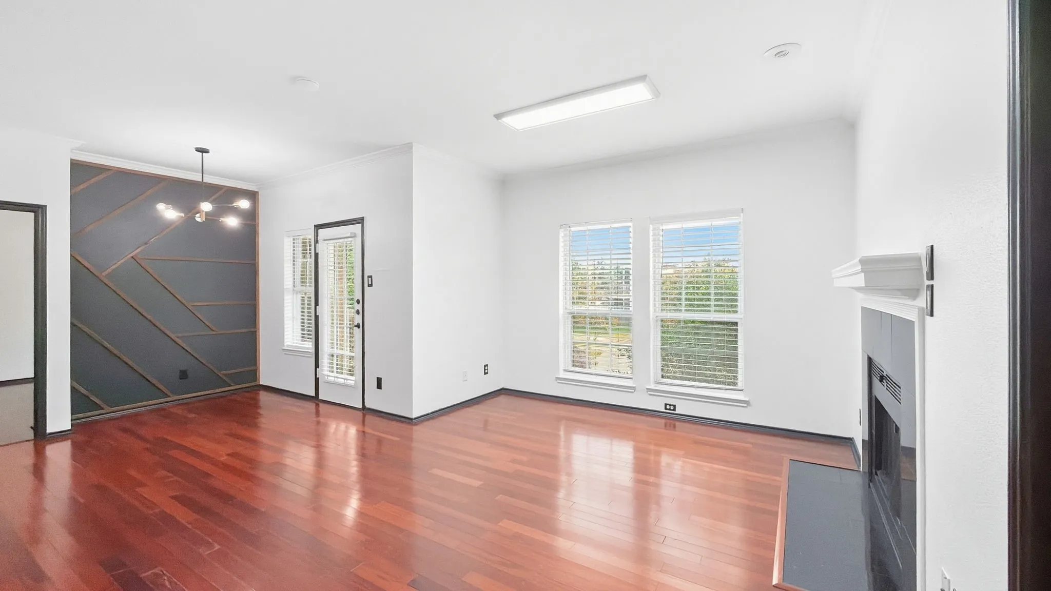 Hardwood flooring throughout, a decorative accent wall with geometric wood trim, a modern chandelier, and a fireplace with a mantel