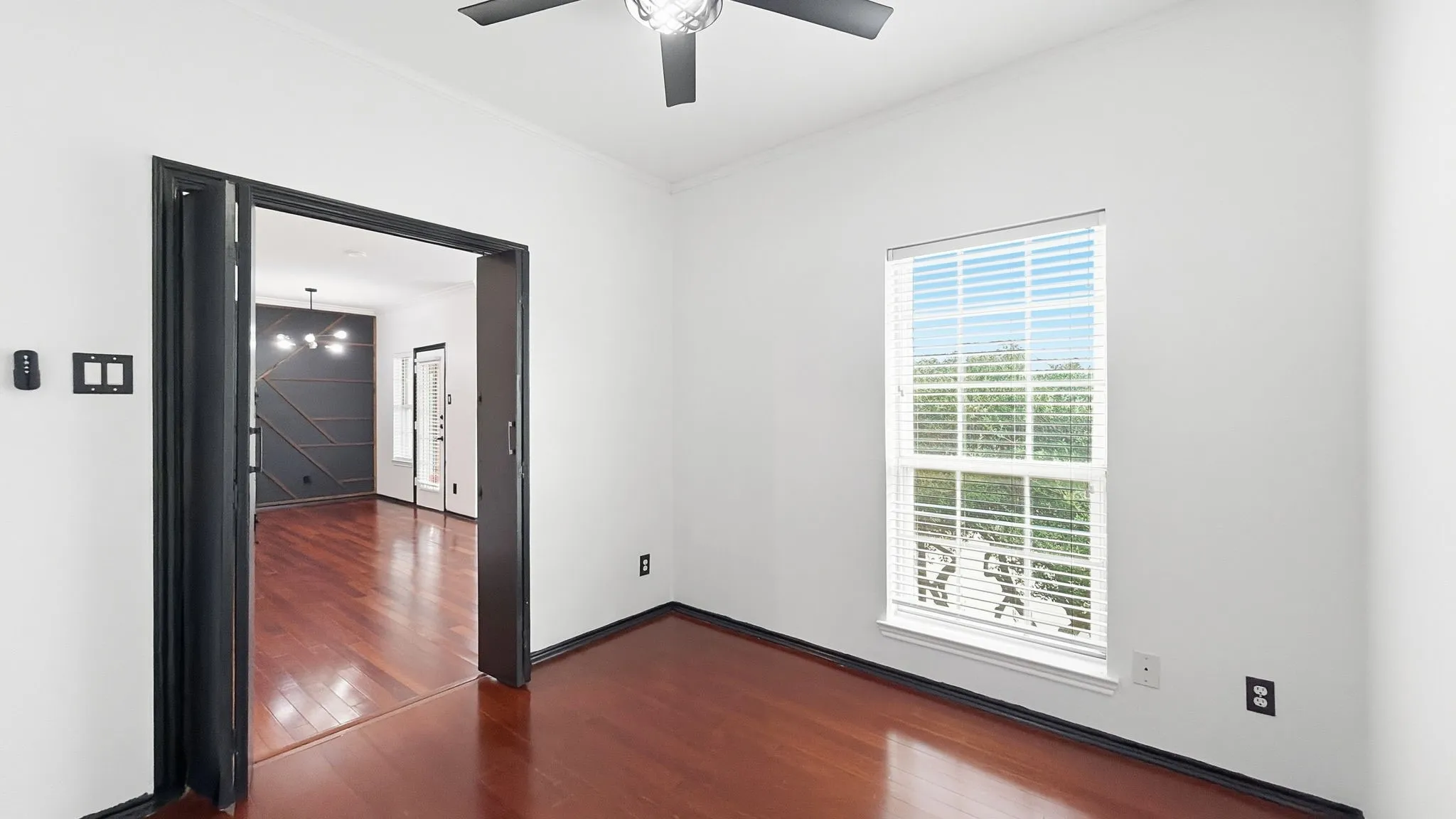 Hardwood flooring throughout, white walls, black trim, ceiling fan with integrated lighting, and a window with blinds