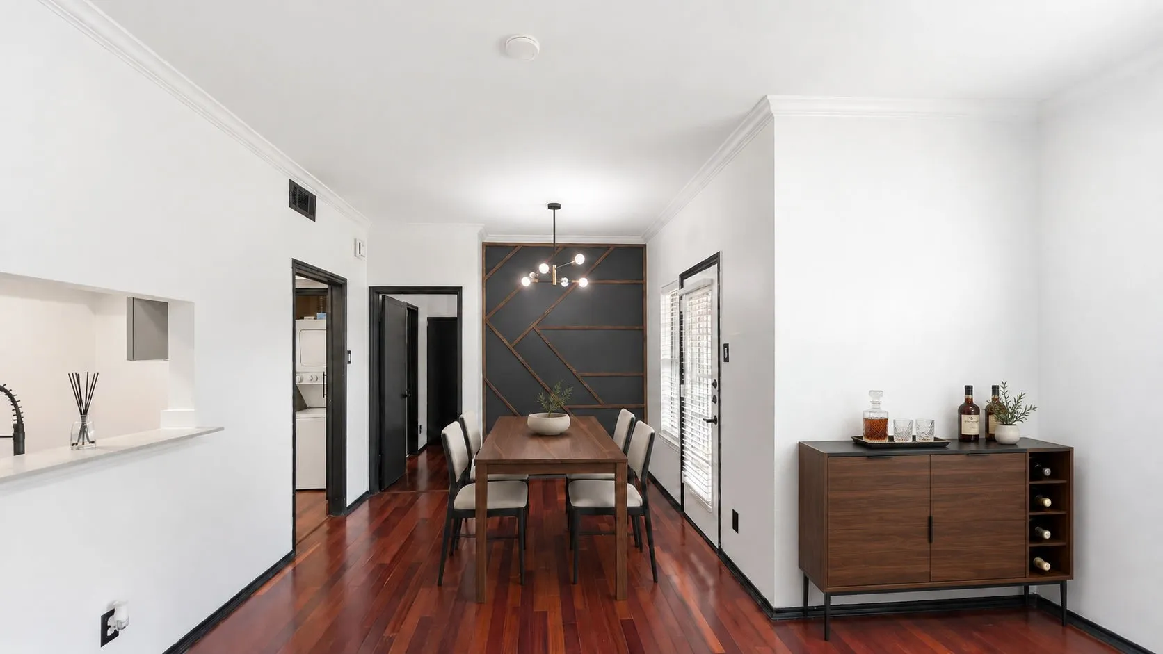 Rich wood-finish flooring, accent wall with geometric paneling, modern ceiling-mounted light fixture, and crown molding virtually staged
