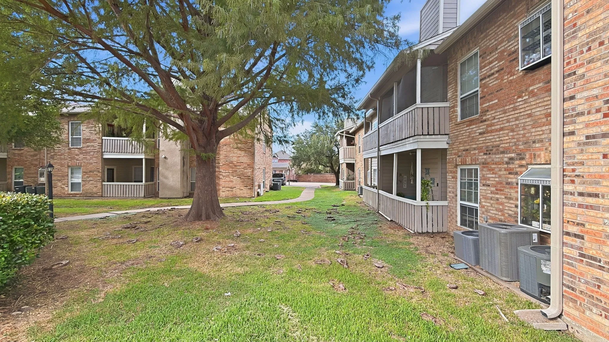 Brick exterior with multiple screened balconies, featuring a mature tree and landscaped shrubbery