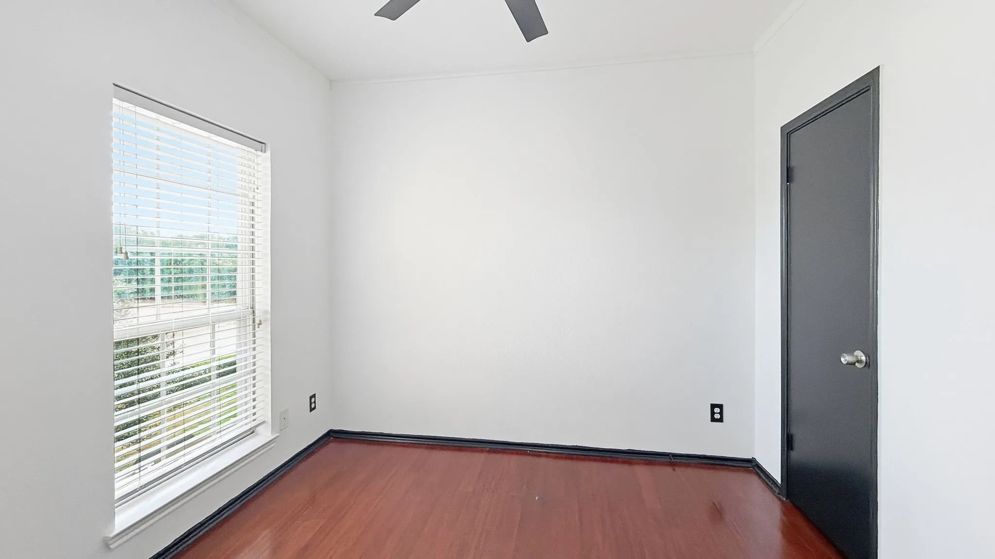 Wood-finish flooring, white walls, white window blinds, dark trim door, ceiling fan