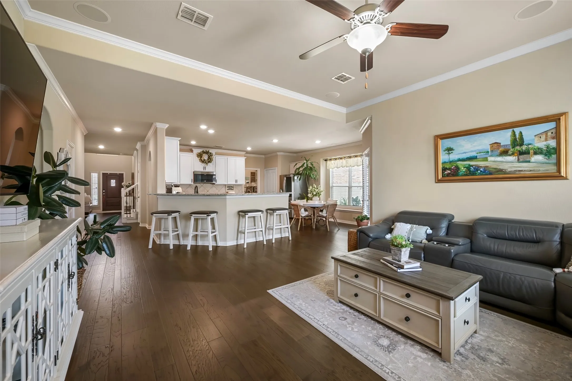 Open-concept living area featuring wood-finish flooring, recessed lighting, crown molding, and a kitchen with white cabinetry and a built-in breakfast bar