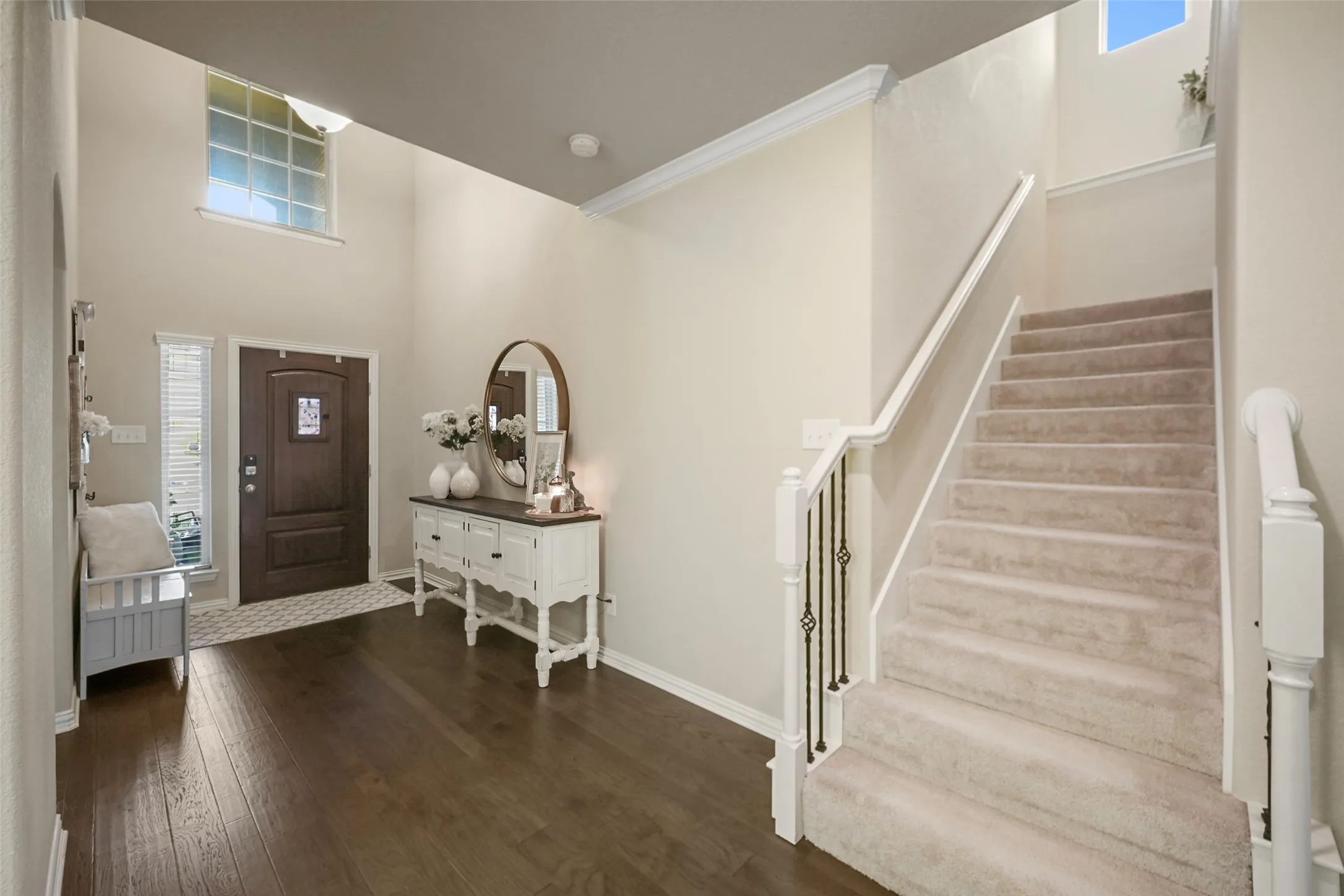 Two-story entryway with wood-finish flooring, a dark wood-paneled door with an arched top, and a carpeted staircase featuring a white railing and wrought iron​​‌​​​​‌​​‌‌​‌‌​​​‌‌​‌​‌​‌​​​‌​​ balusters