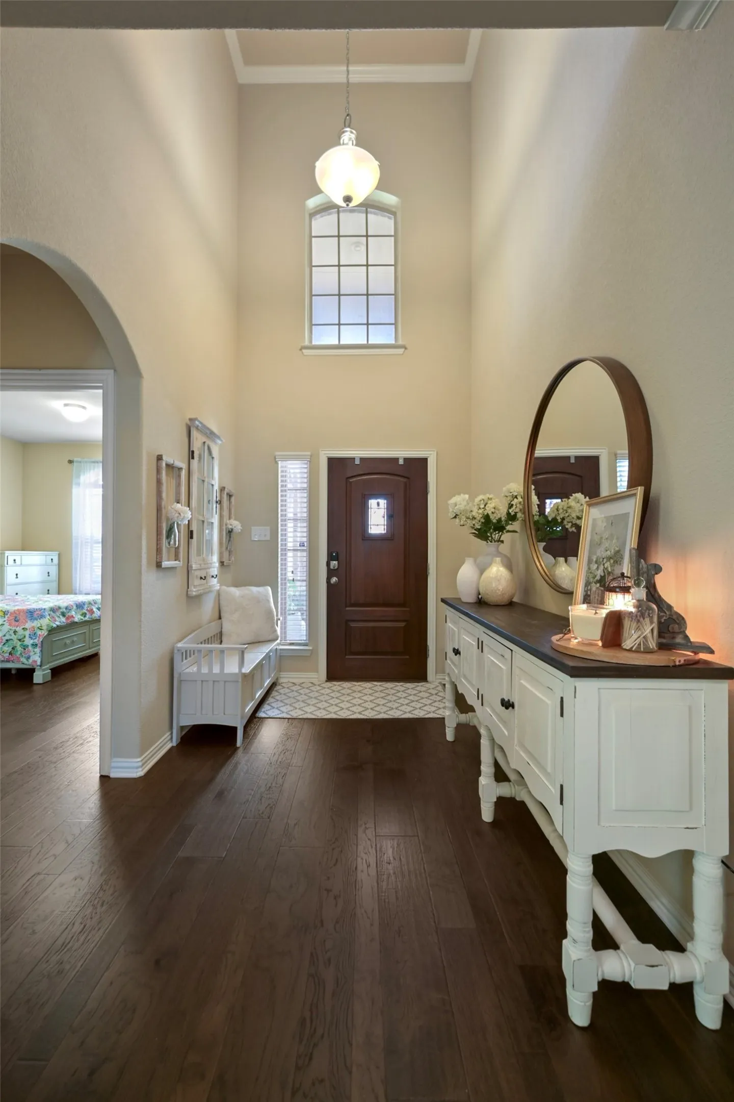 Two-story foyer featuring dark wood-finish flooring, a tall arched window, a decorative pendant light fixture, and an arched entryway