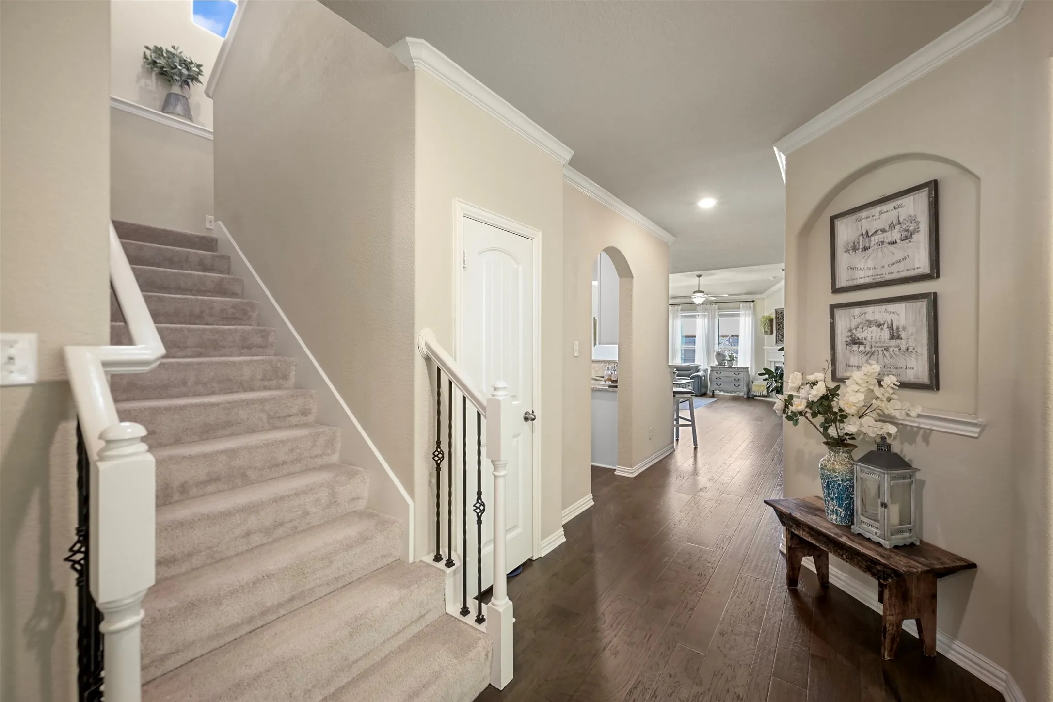 Hardwood-style flooring extends through the hallway, complemented by a carpeted staircase with white balusters and wrought iron spindles