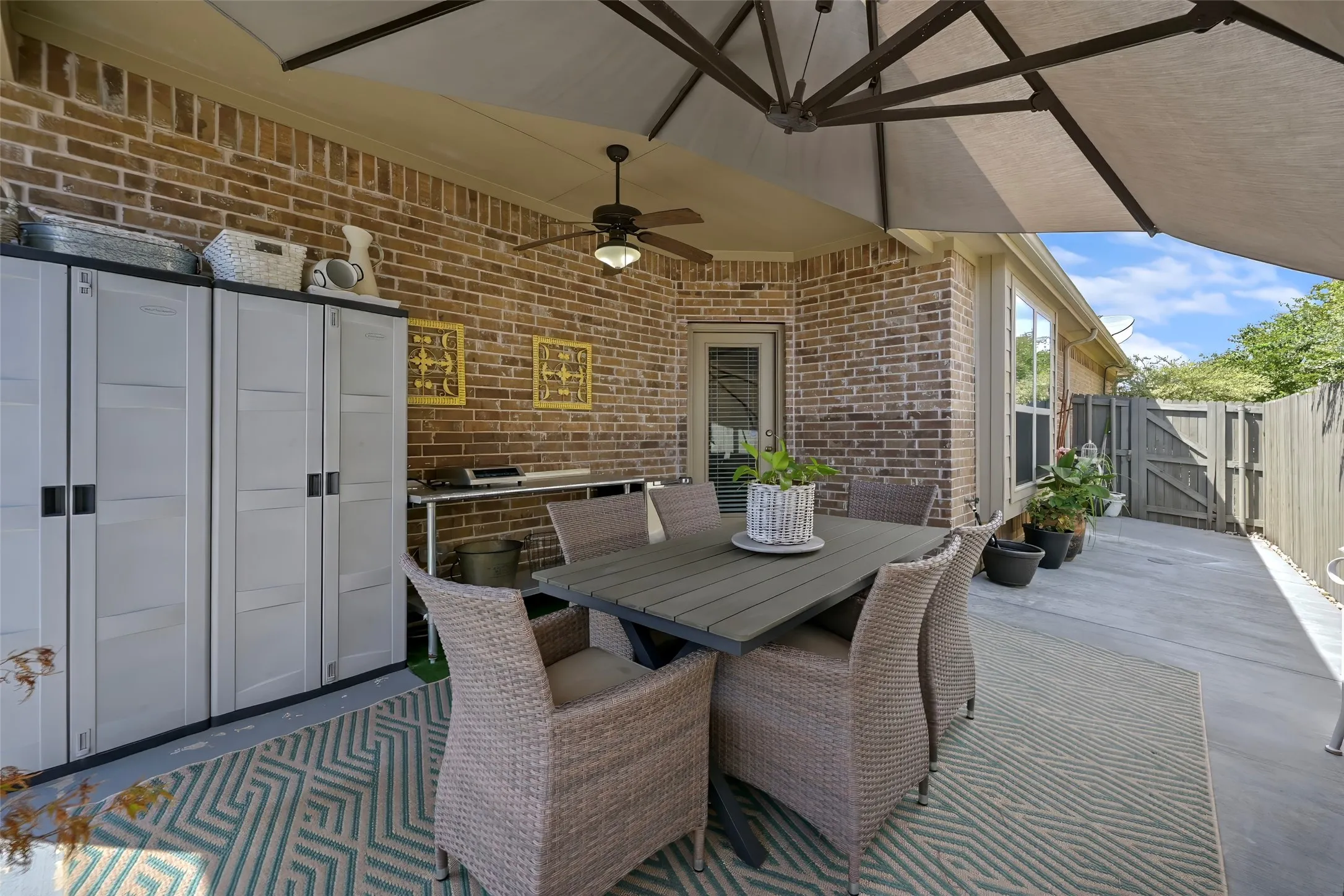 Brick exterior with a covered patio, ceiling fan, and privacy fence