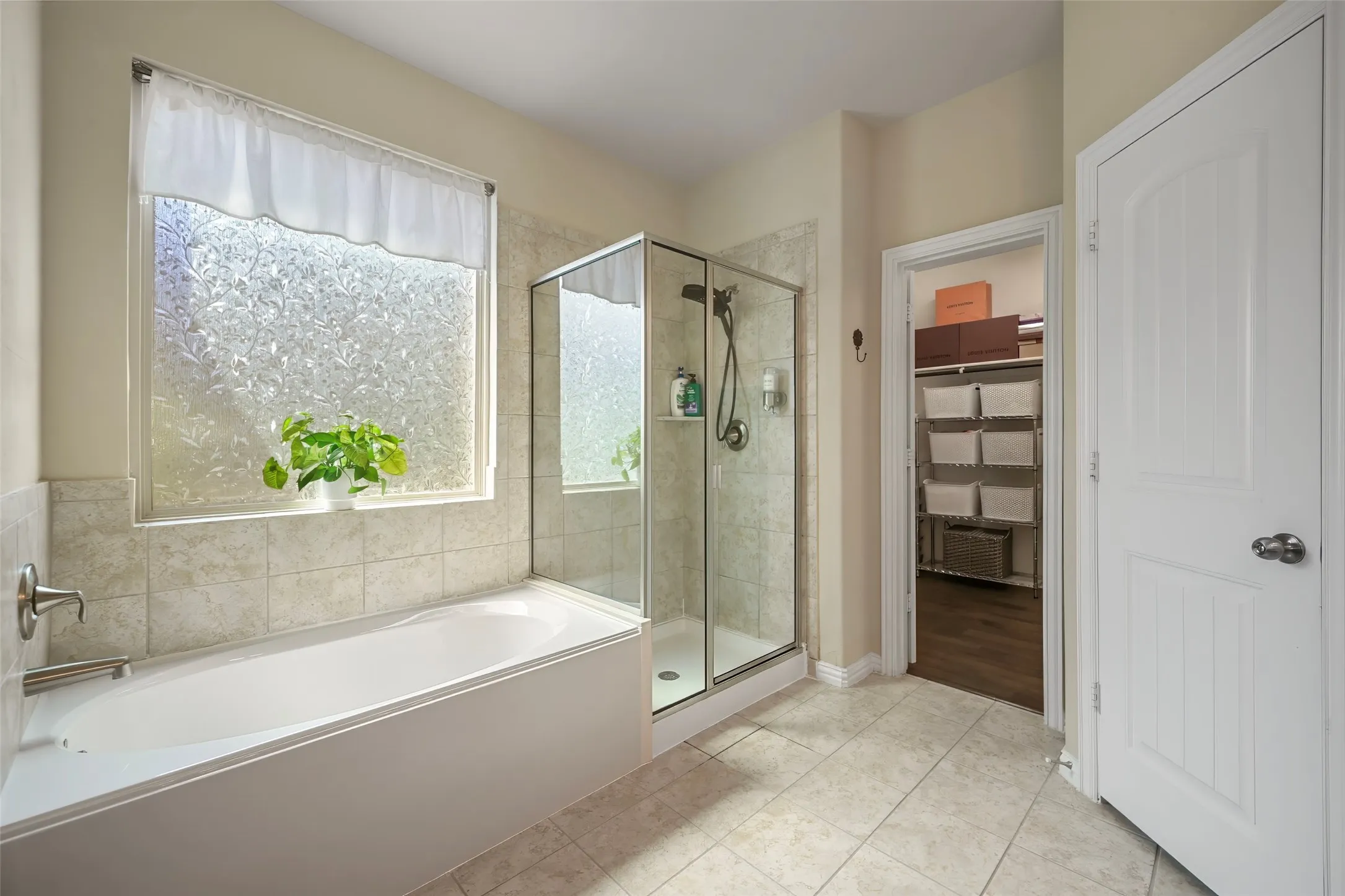 Soaking tub with tile surround, glass-enclosed shower, frosted window, and tile flooring