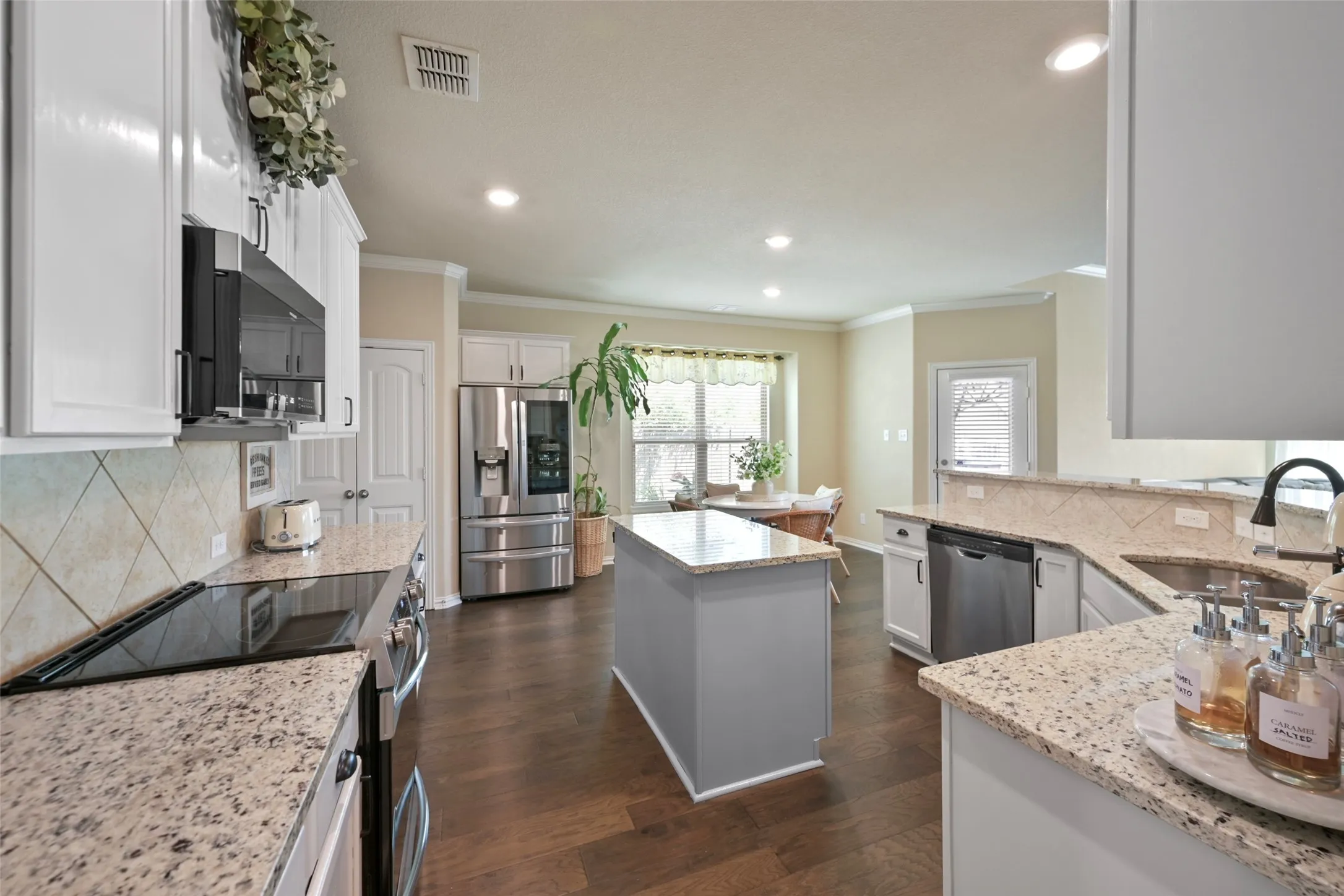 Kitchen featuring granite countertops, wood-finish flooring, white cabinetry, a central island, and stainless steel appliances
