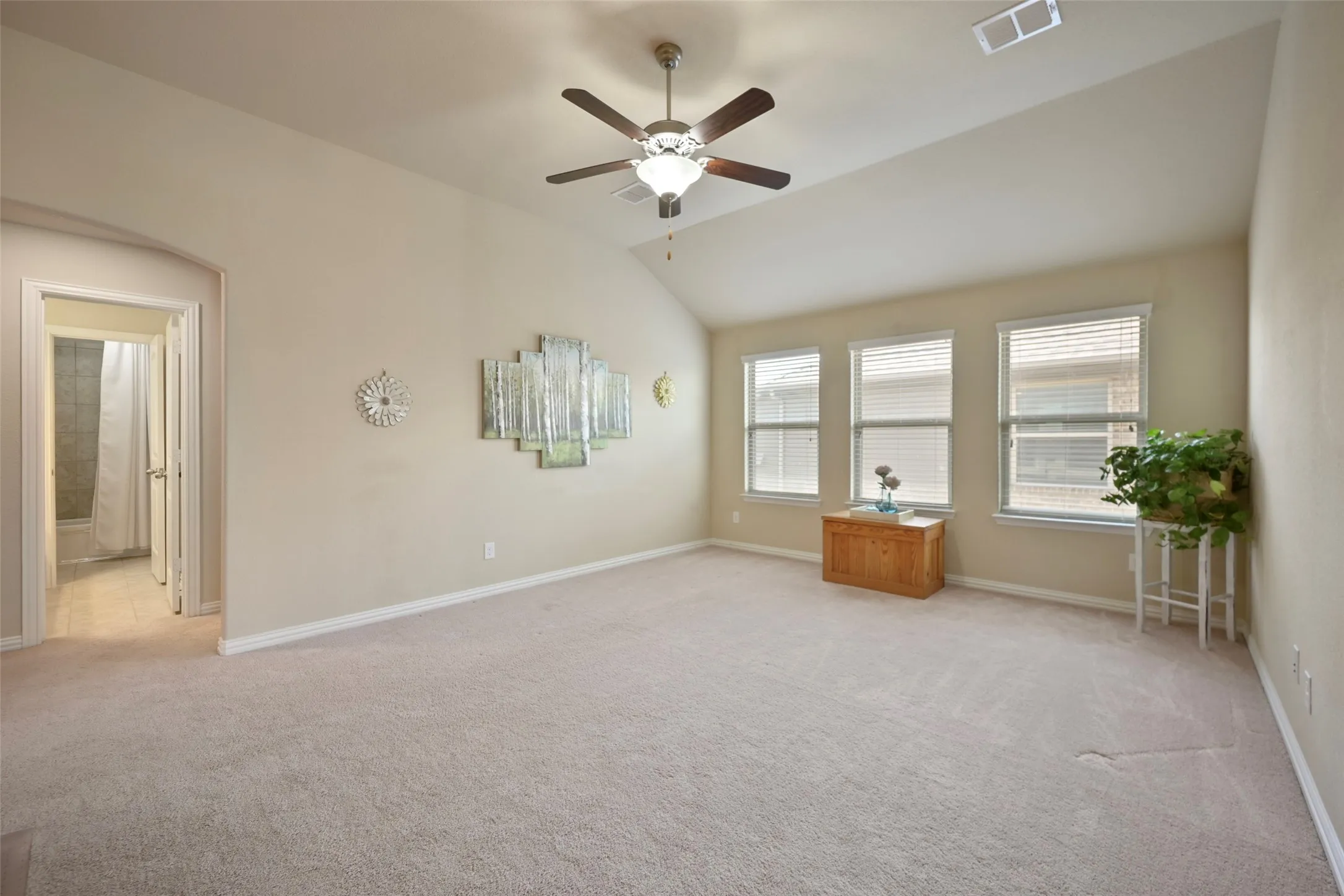 Spacious carpeted room featuring a vaulted ceiling with a ceiling fan, multiple windows with blinds, and an arched doorway