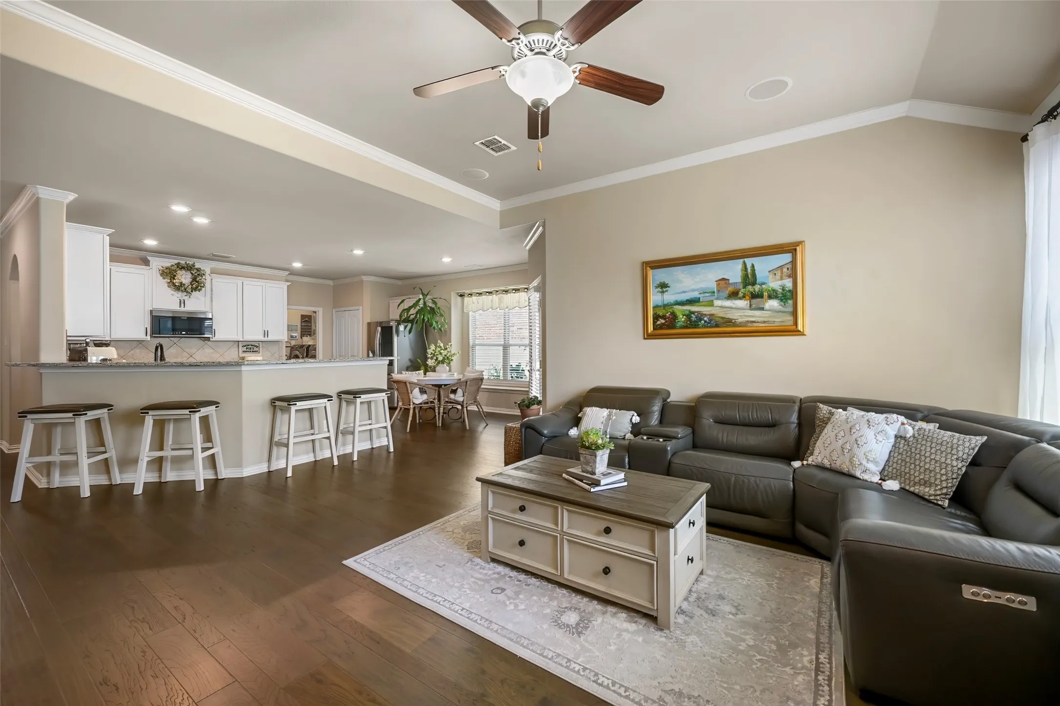 Open-concept living area with dark wood-finish flooring, a kitchen island with built-in seating, and a vaulted ceiling with a fan