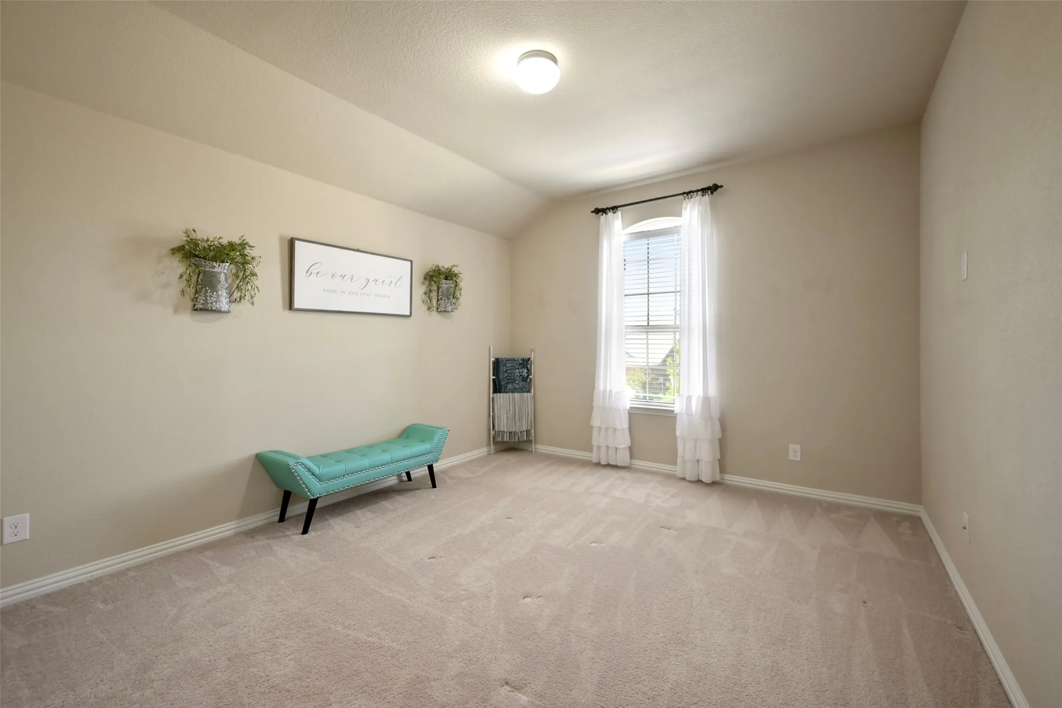 Spacious room featuring vaulted ceilings, neutral-toned walls, and an arched window