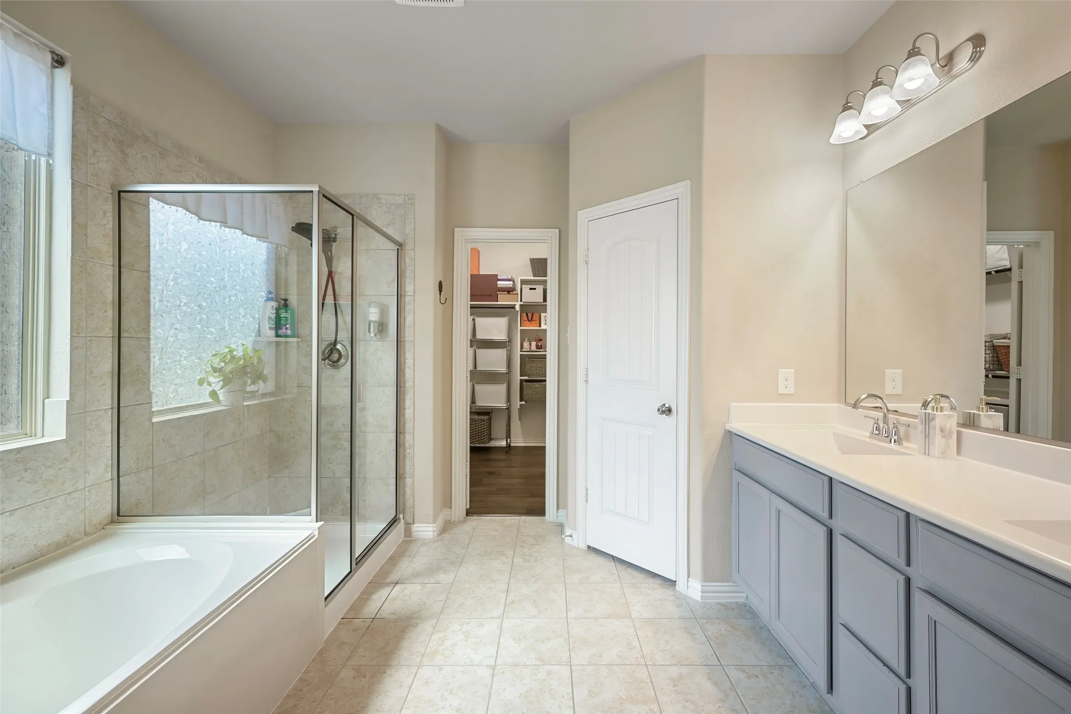 Double vanity with light gray cabinetry, built-in bathtub, glass-enclosed shower, and tile flooring