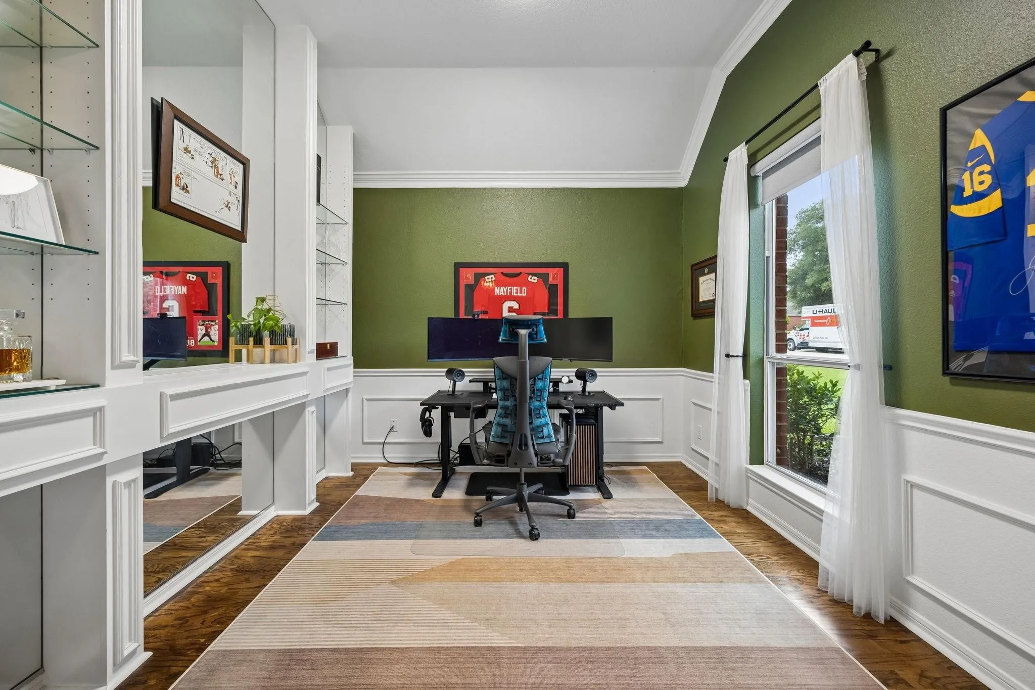 Built-in shelving with glass inserts, dedicated desk area, wood-finish flooring, accent wall, and crown molding