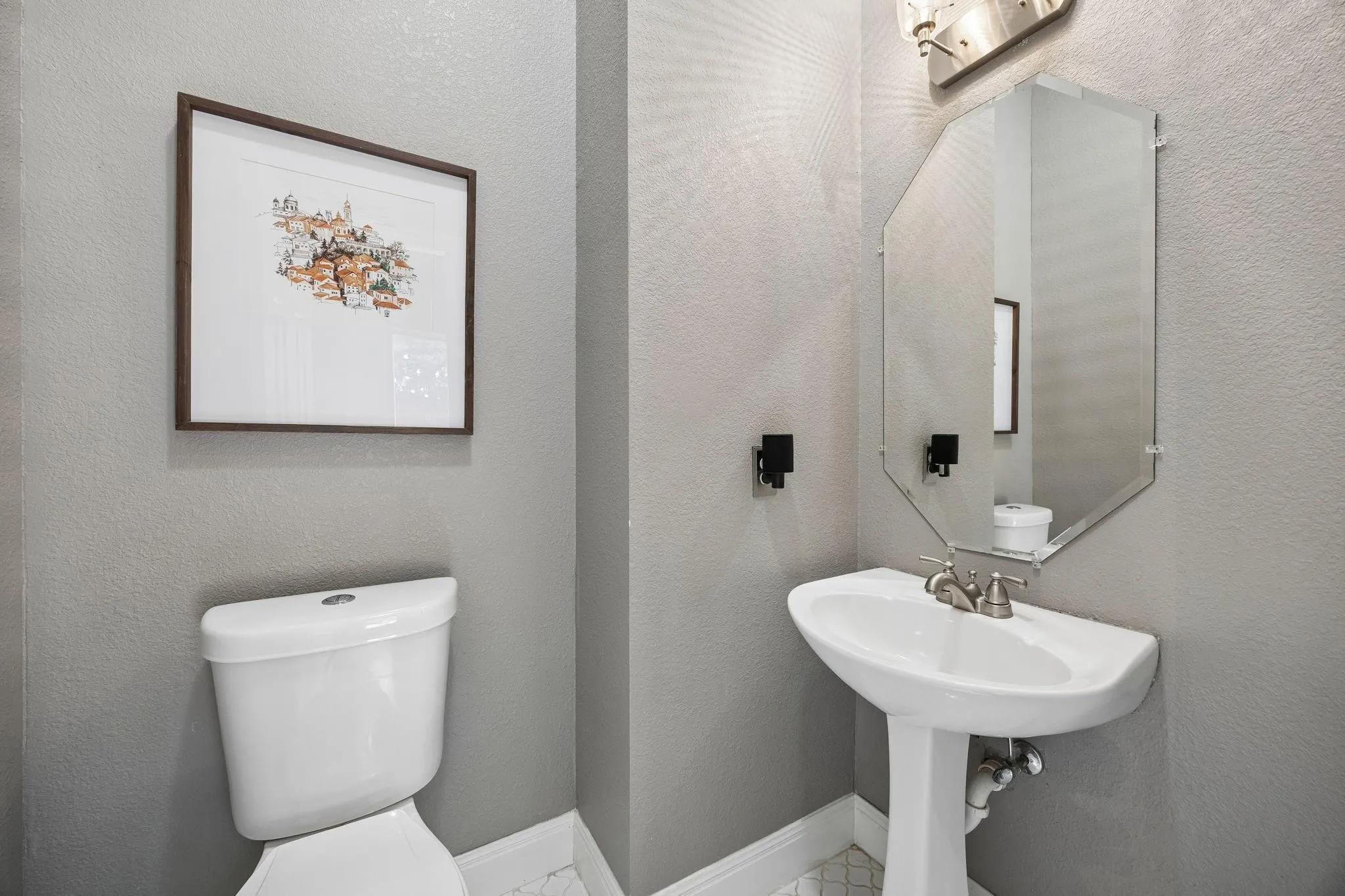 Pedestal sink with brushed nickel faucet, beveled mirror, and wall-mounted vanity lighting