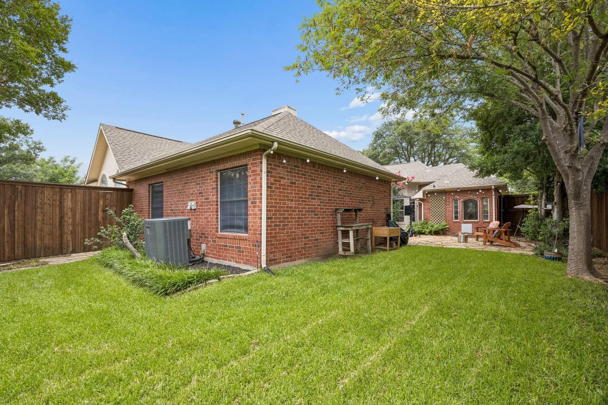 Expansive lawn area with a wood privacy fence, mature trees, and a brick exterior building