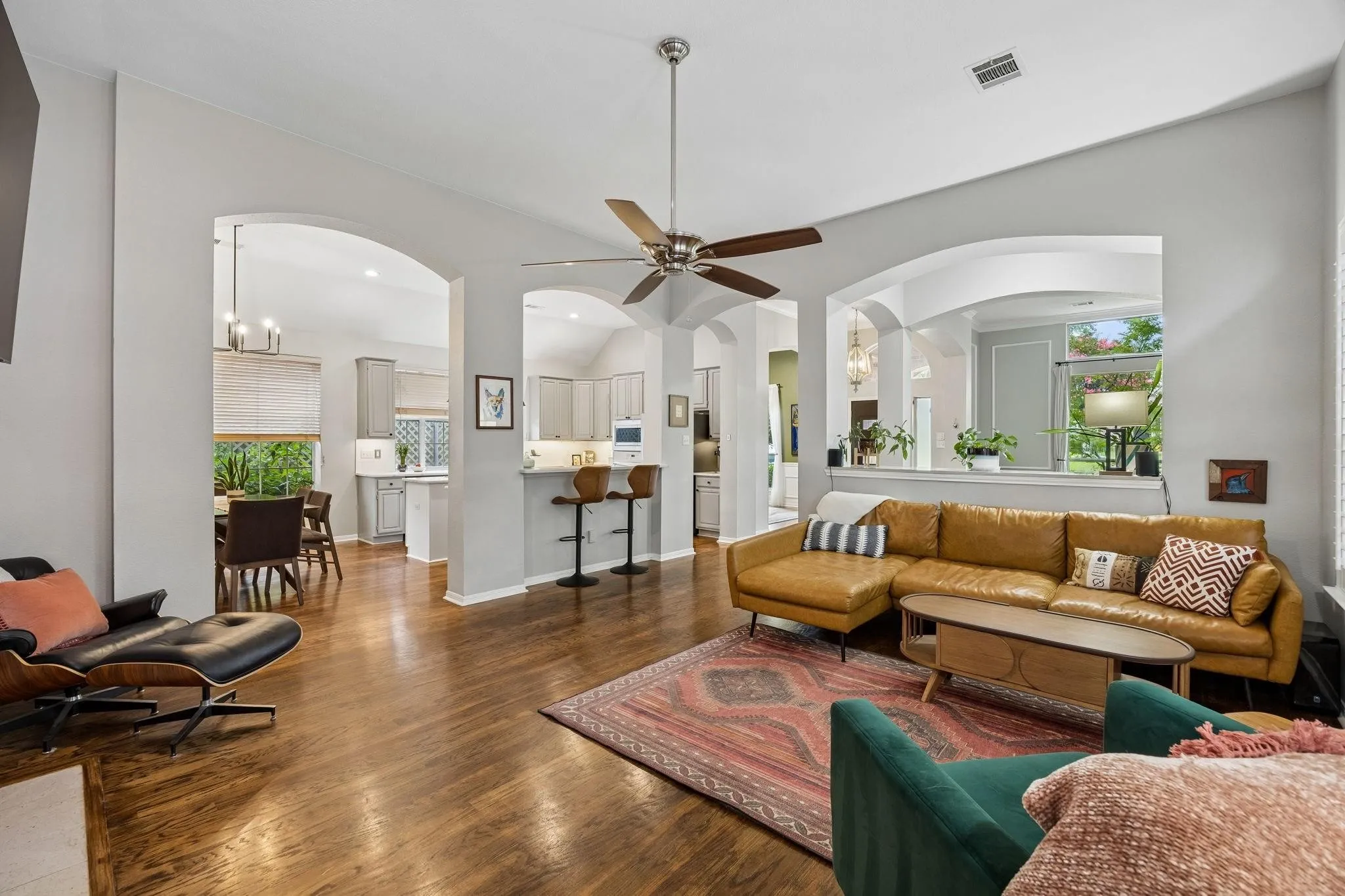 Hardwood flooring with a polished finish, arched doorways, vaulted ceiling, and a ceiling fan with light fixture