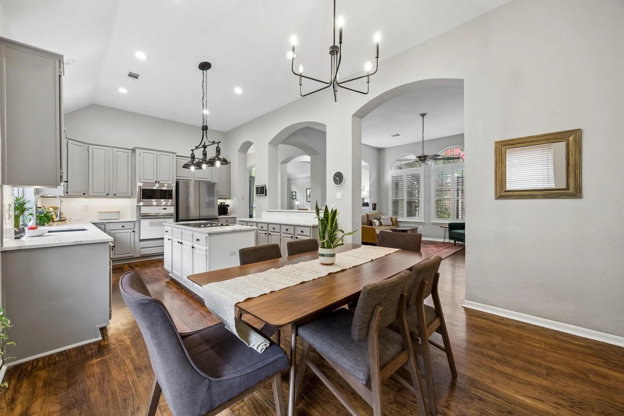 Open-concept layout featuring vaulted ceilings, wood-finish flooring, arched doorways, a kitchen island with built-in cooktop, and stainless steel appliances