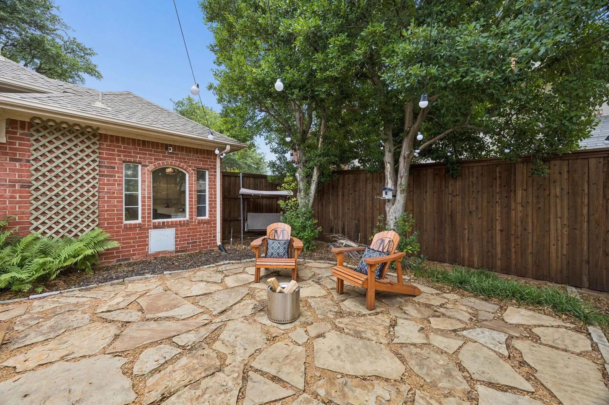 Stone patio featuring a brick exterior with an arched window, mature trees, and a wood privacy fence