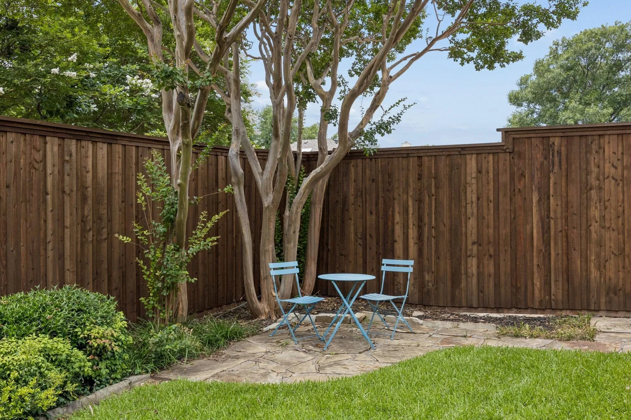 Manicured lawn with a stone patio, mature trees, and a privacy fence