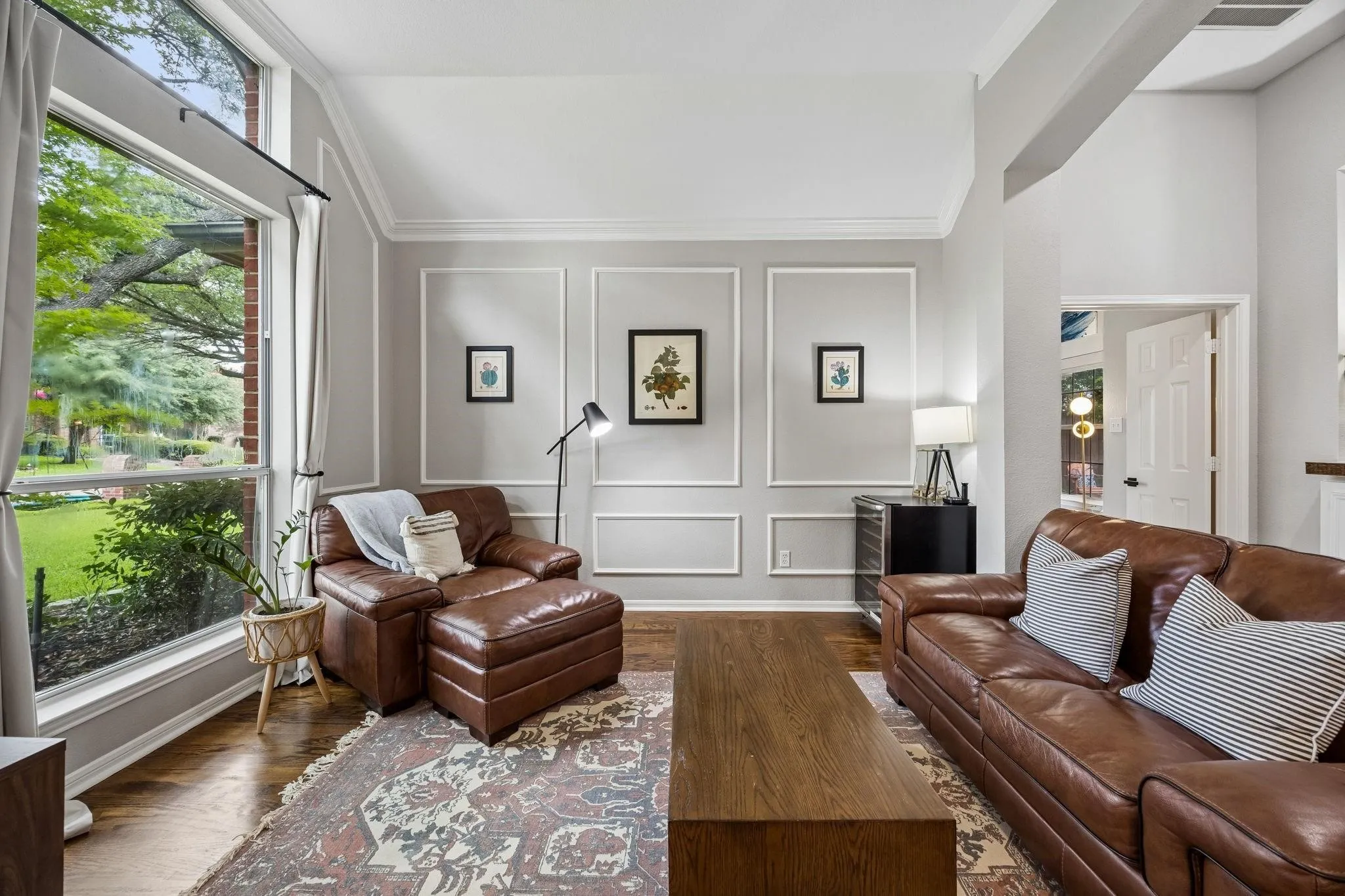 Expansive windows allowing natural light, vaulted ceiling, decorative wall paneling, and wood-finish flooring