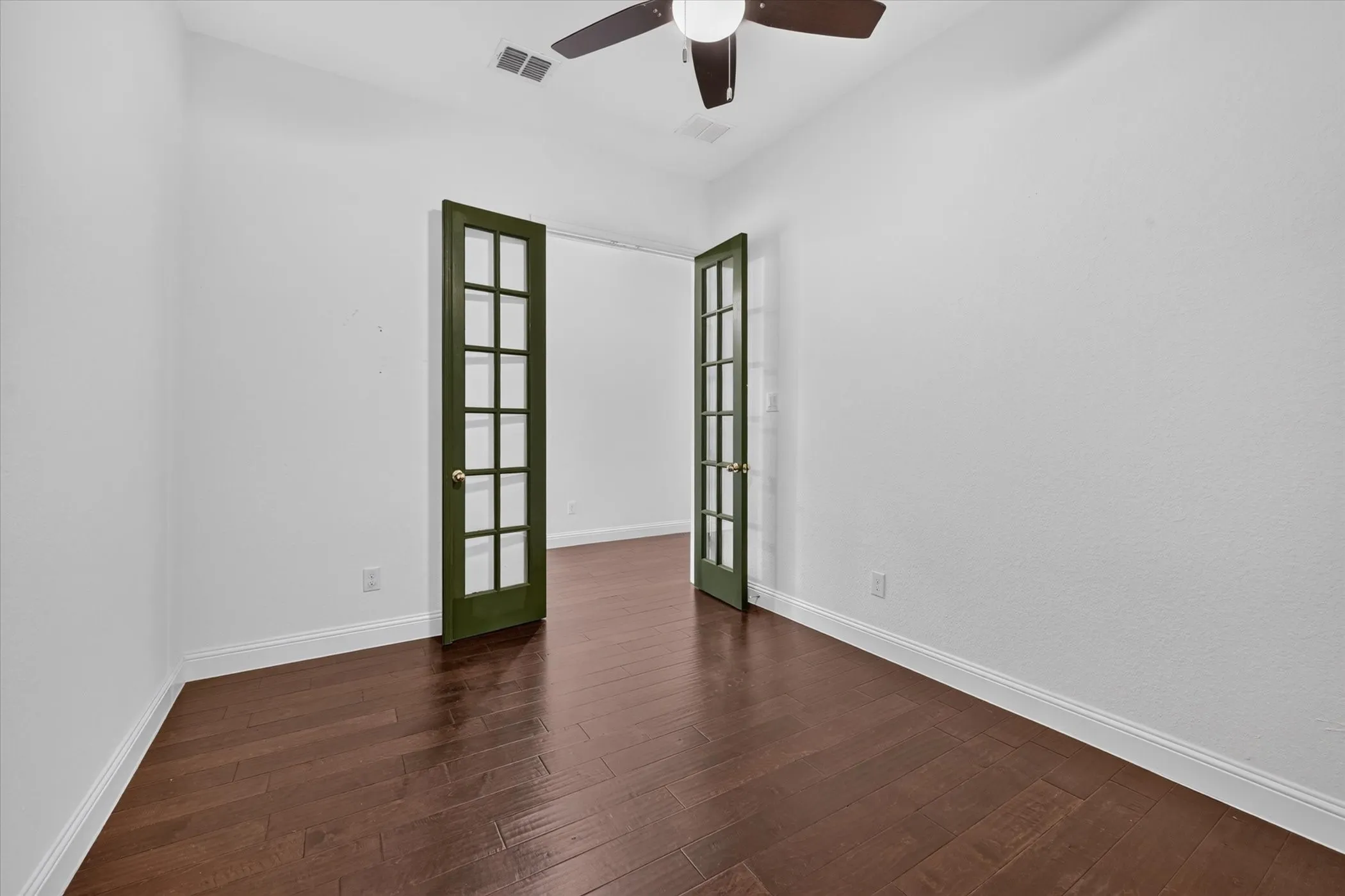 Wood-finish flooring throughout the space, featuring white walls, white trim, and dark green French doors with glass panels