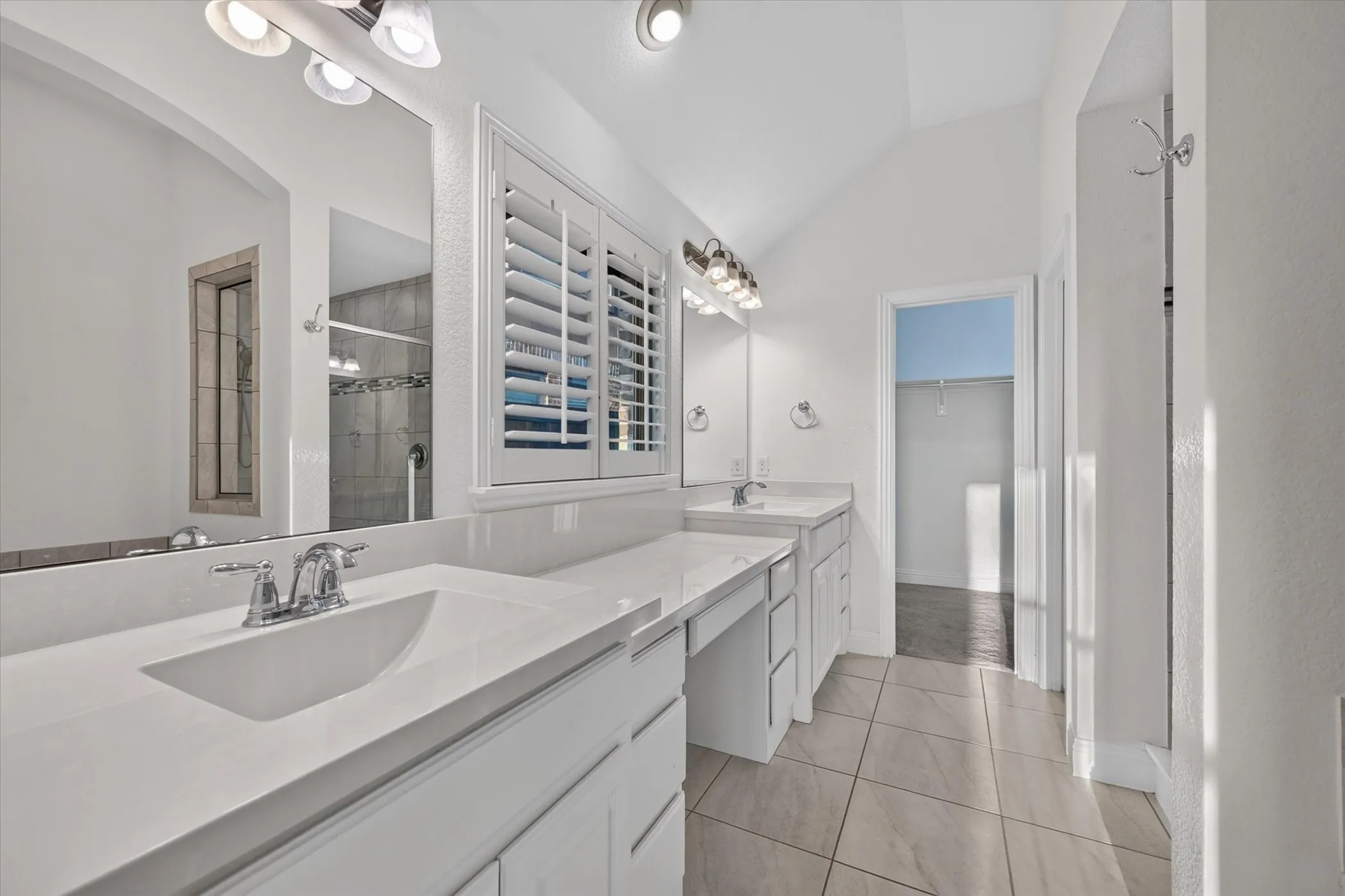 Dual vanity with chrome fixtures and integrated sinks, white cabinetry, plantation shutters, and tiled flooring