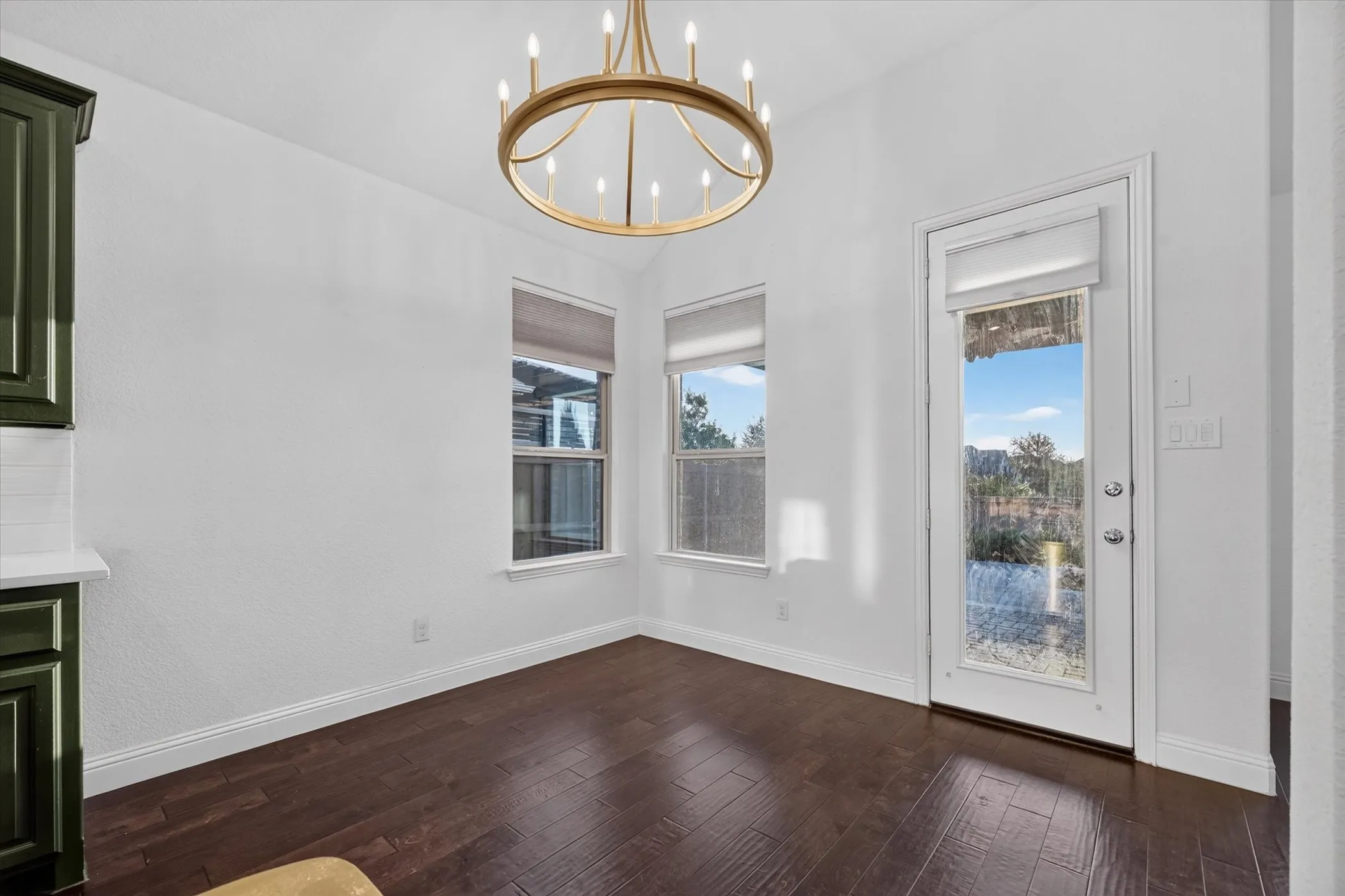 Hardwood-finish flooring, a gold-tone chandelier, two double-hung windows, white walls, and a glass-paneled exterior door