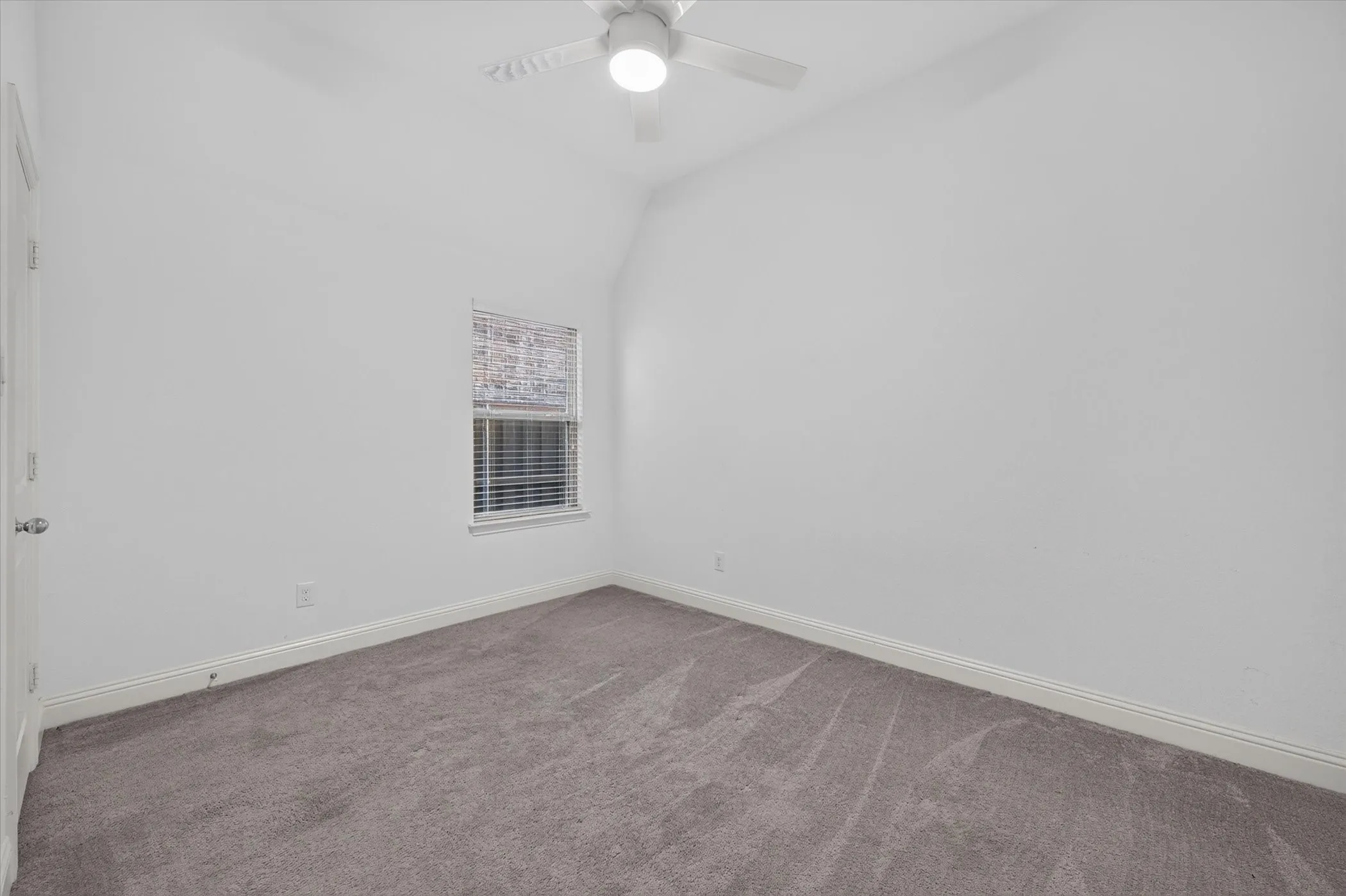 Vaulted ceiling featuring a ceiling fan with light, neutral tone carpeting, and a single window with blinds