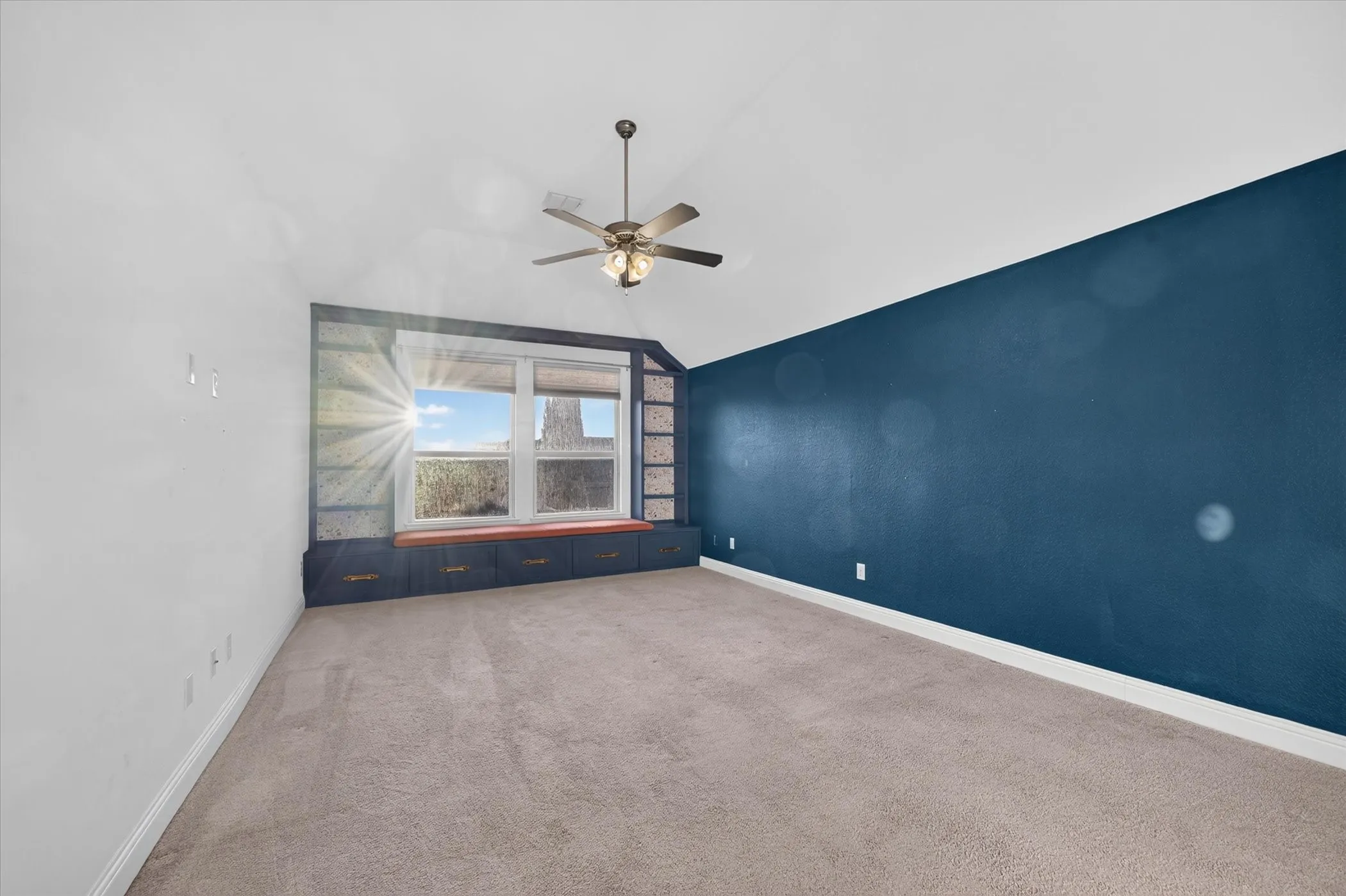 Vaulted ceiling with a ceiling fan, built-in window seating with storage, integrated shelving, and carpet flooring