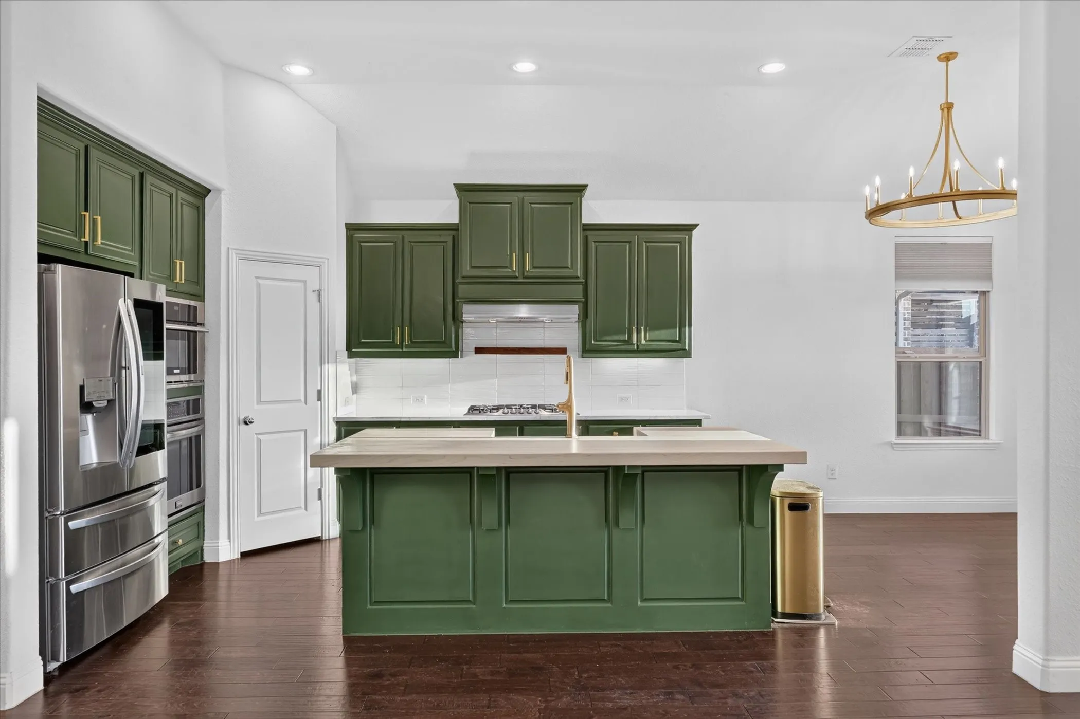 Kitchen featuring dark green cabinetry, stainless steel appliances, a center island with countertop, a white subway tile backsplash, and wood-finish flooring