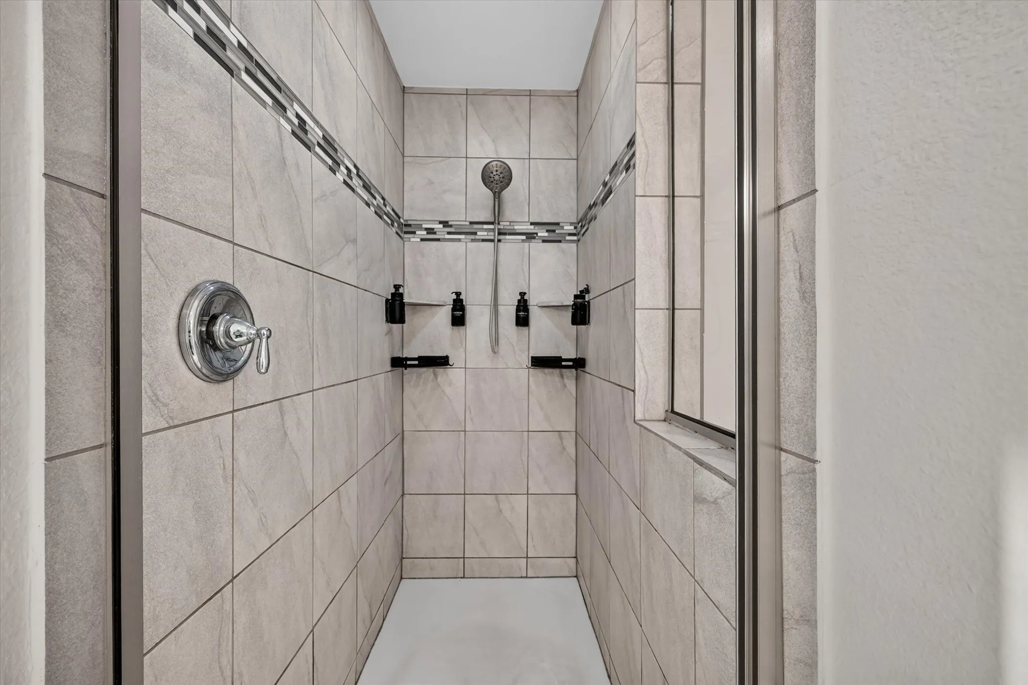 Tiled shower with a decorative mosaic accent band, equipped with a handheld shower head and multiple built-in shelving units