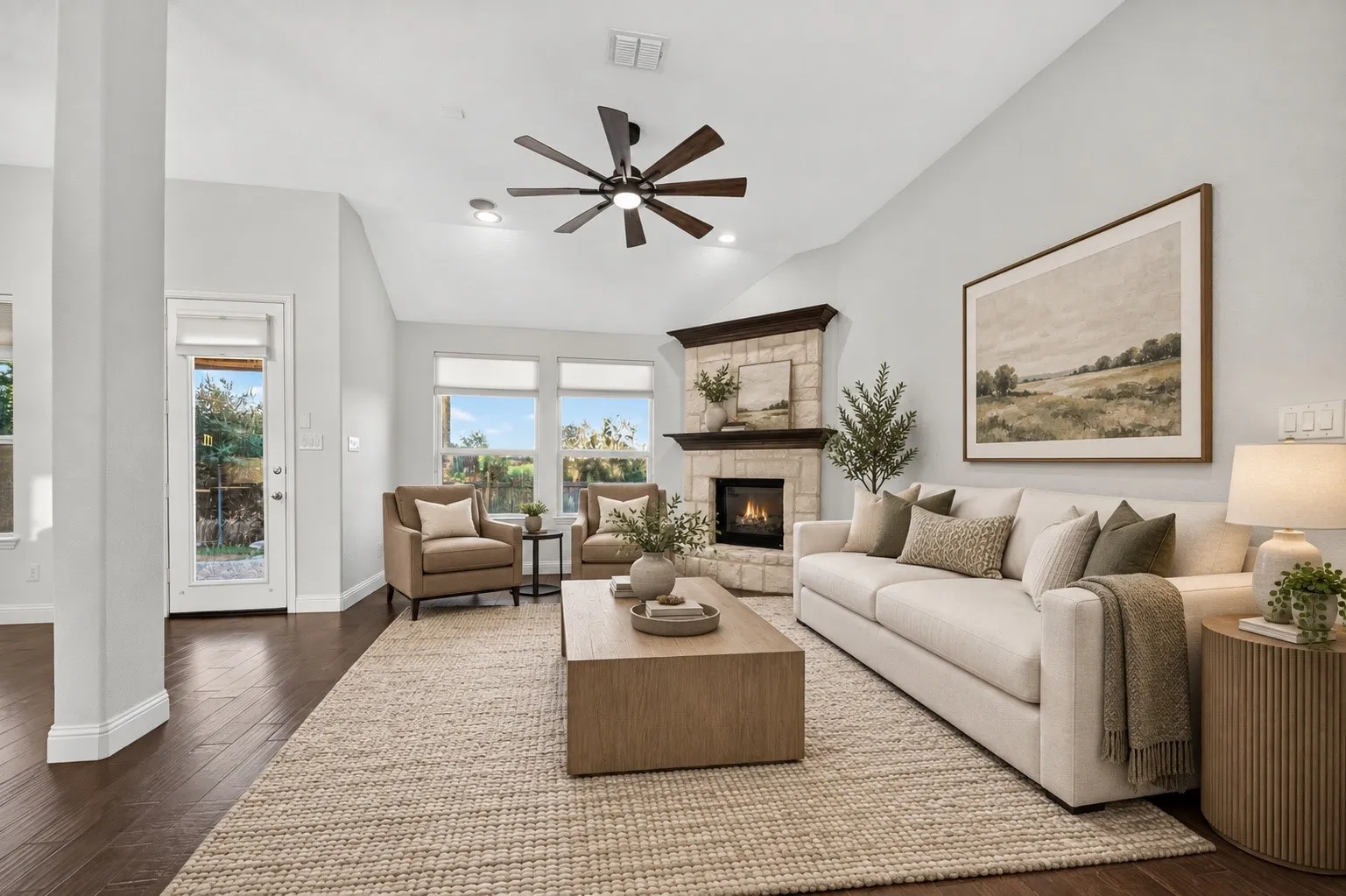 Vaulted ceiling with a ceiling fan, stone fireplace with a dark wood mantel, dark wood-finish flooring, and multiple windows