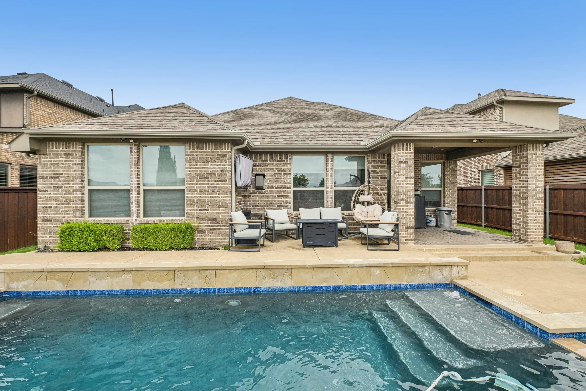 Brick exterior featuring a covered patio, outdoor swimming pool with steps, and concrete patio surround