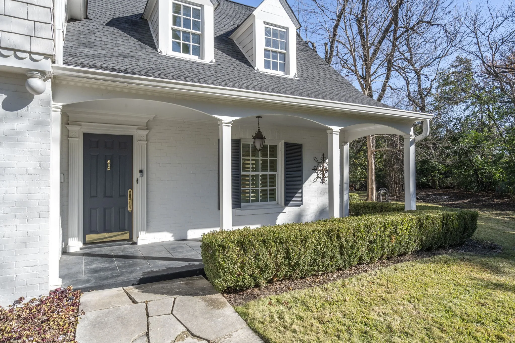 Property entrance with a porch, a shingled roof, brick siding, and a yard