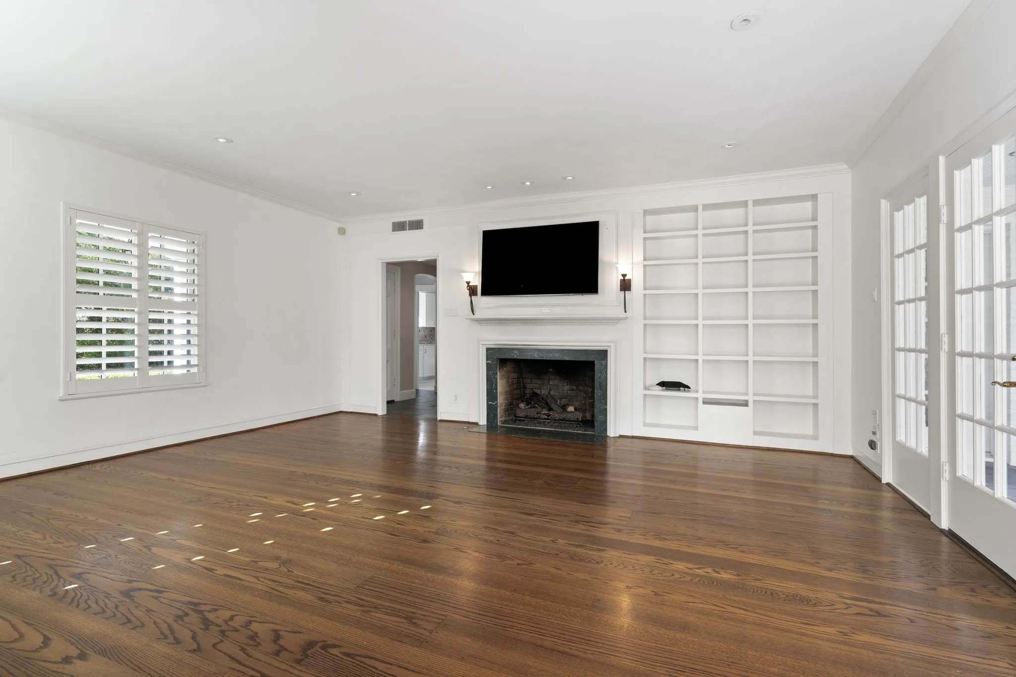 Unfurnished living room with built in features, a fireplace with flush hearth, dark wood-type flooring, and ornamental molding