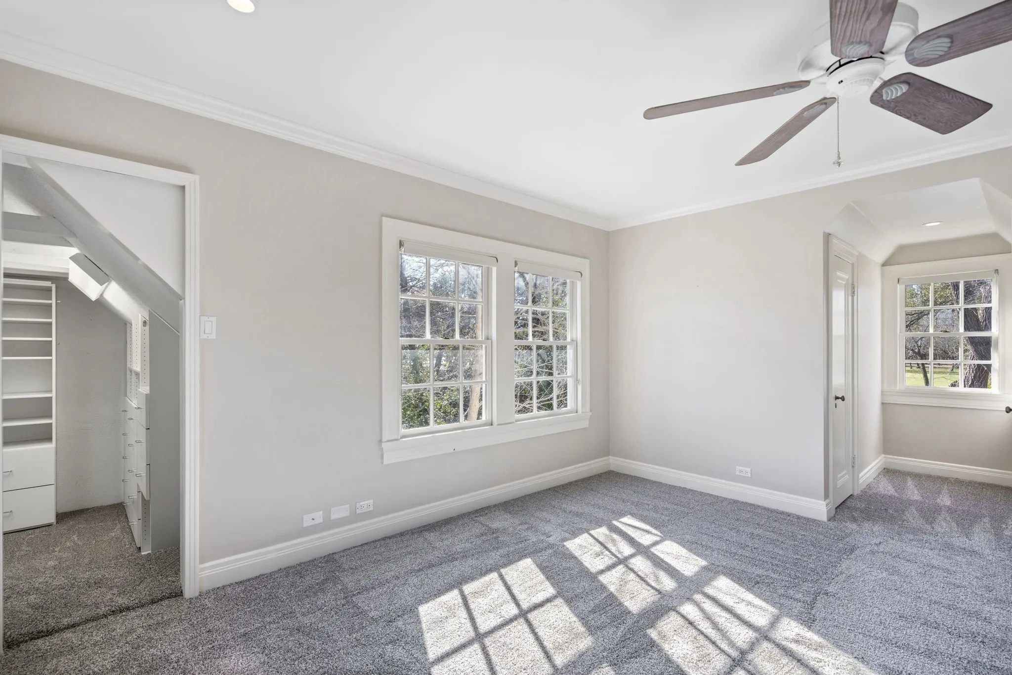 Unfurnished bedroom featuring carpet, ornamental molding, a ceiling fan, and a walk in closet