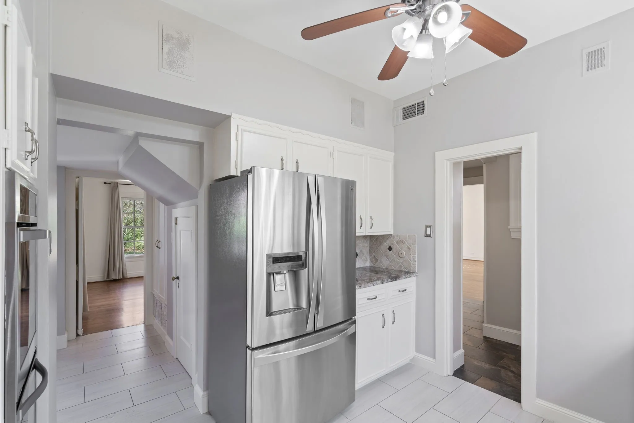 Kitchen featuring stainless steel appliances, white cabinets, ceiling fan, and light stone countertops