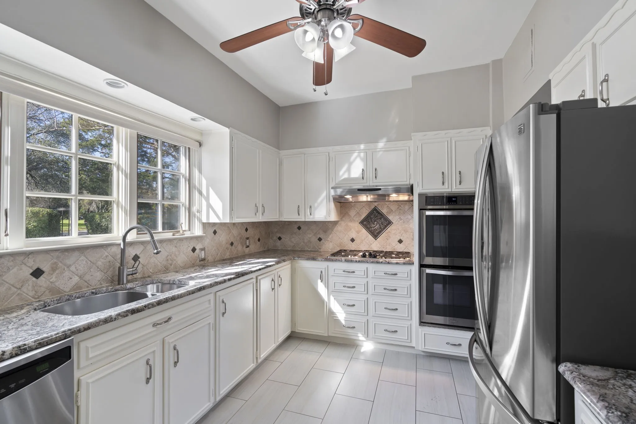 Kitchen with stainless steel appliances, light stone countertops, and white cabinetry
