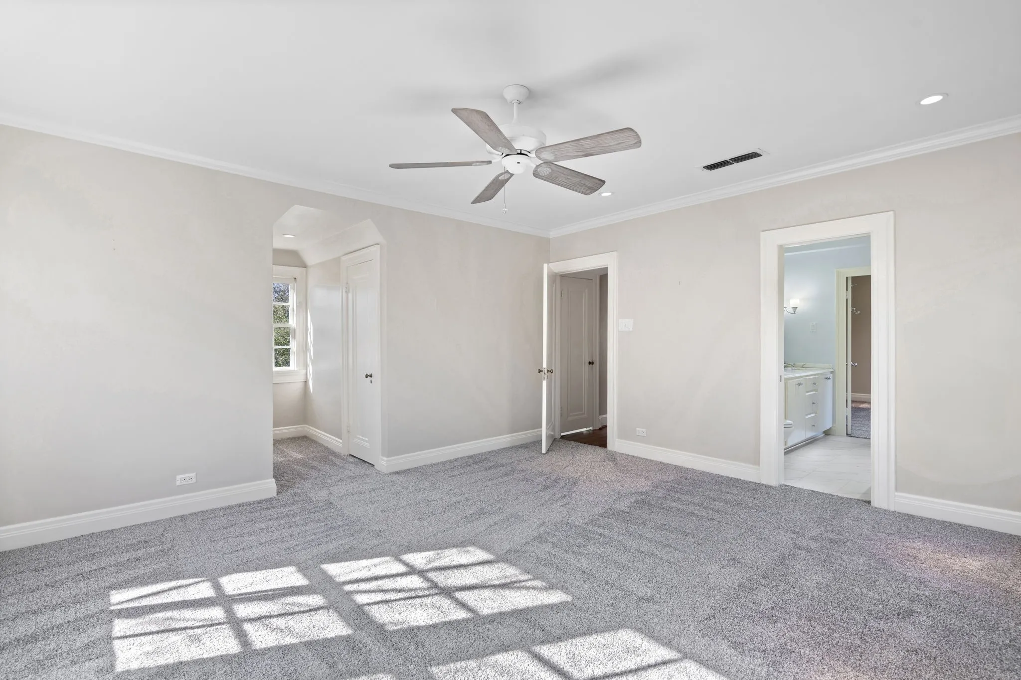 Unfurnished bedroom with light colored carpet, ornamental molding, arched walkways, a ceiling fan, and ensuite bath