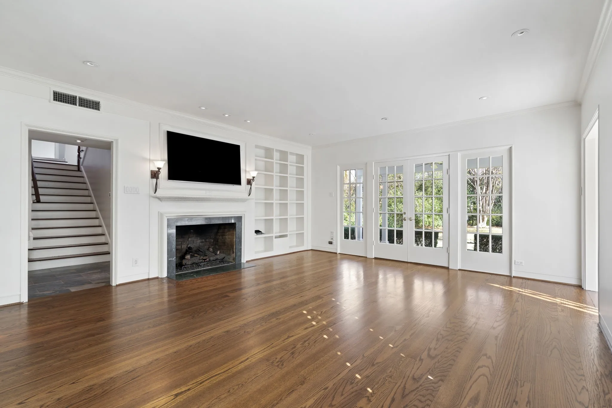 Unfurnished living room with french doors, plenty of natural light, dark wood-style floors, built in features, and crown molding