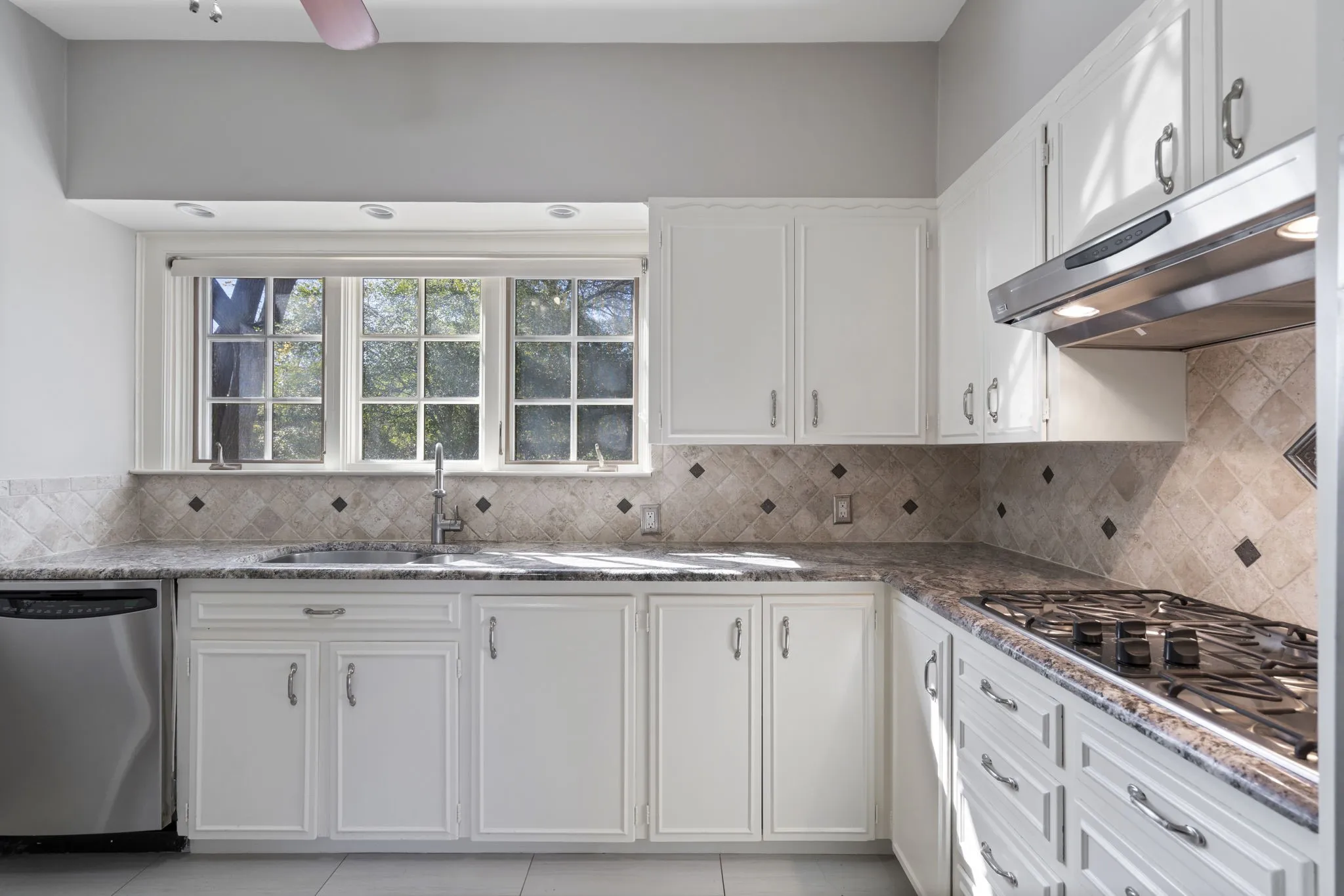 Kitchen with stainless steel appliances, white cabinetry, light tile patterned floors, and dark stone counters