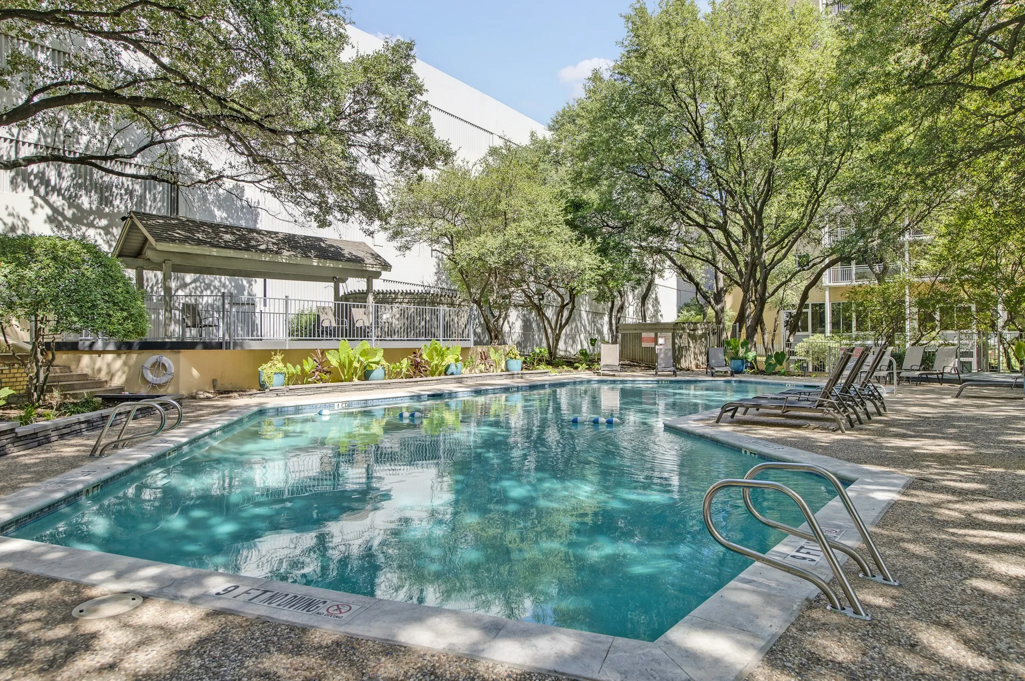Swimming pool with integrated steps, surrounded by mature trees, a shaded gazebo, and lounge seating